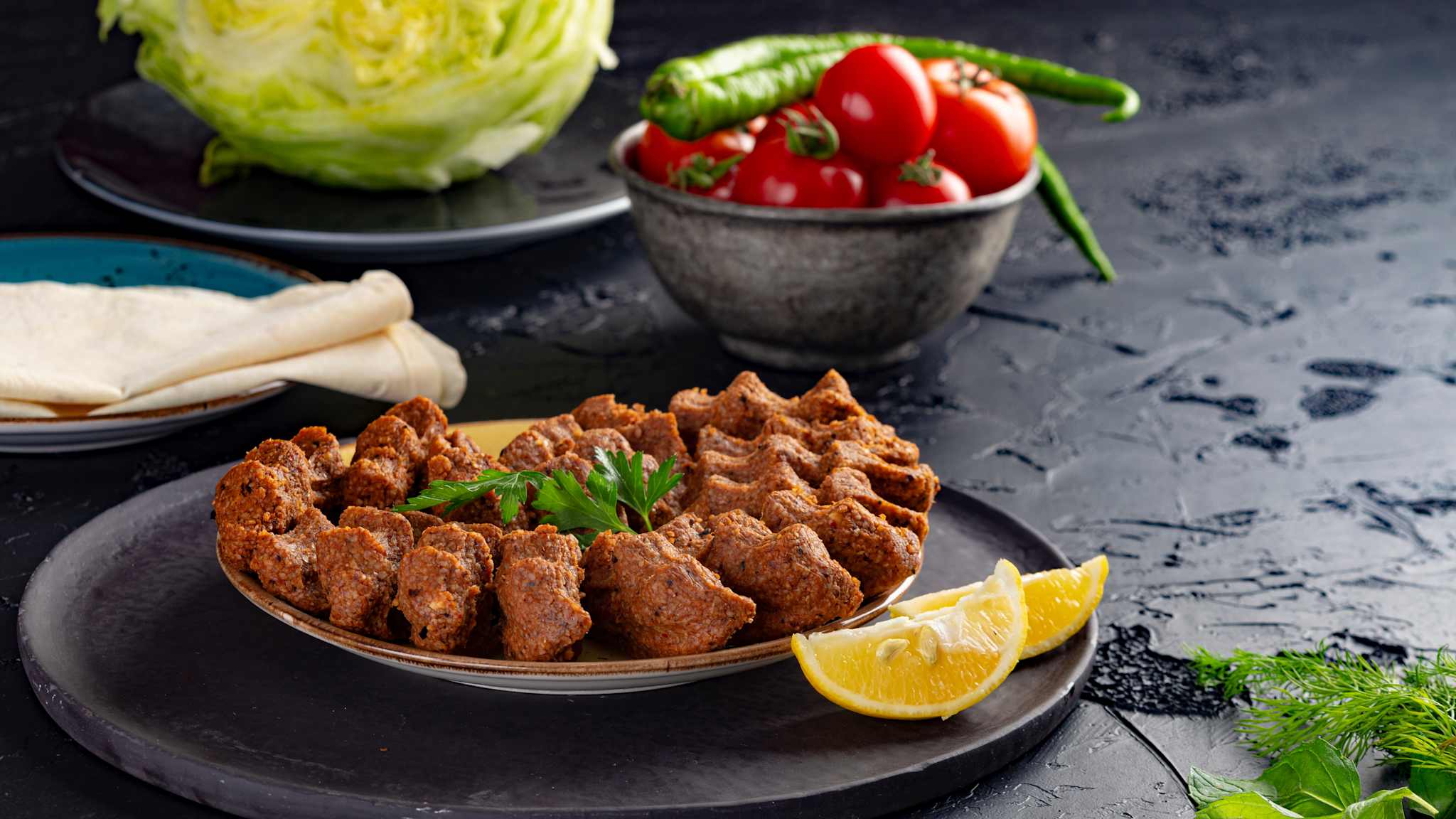 Teller mit Köfte, im Hintergrund verschiedenes Salatgemüse