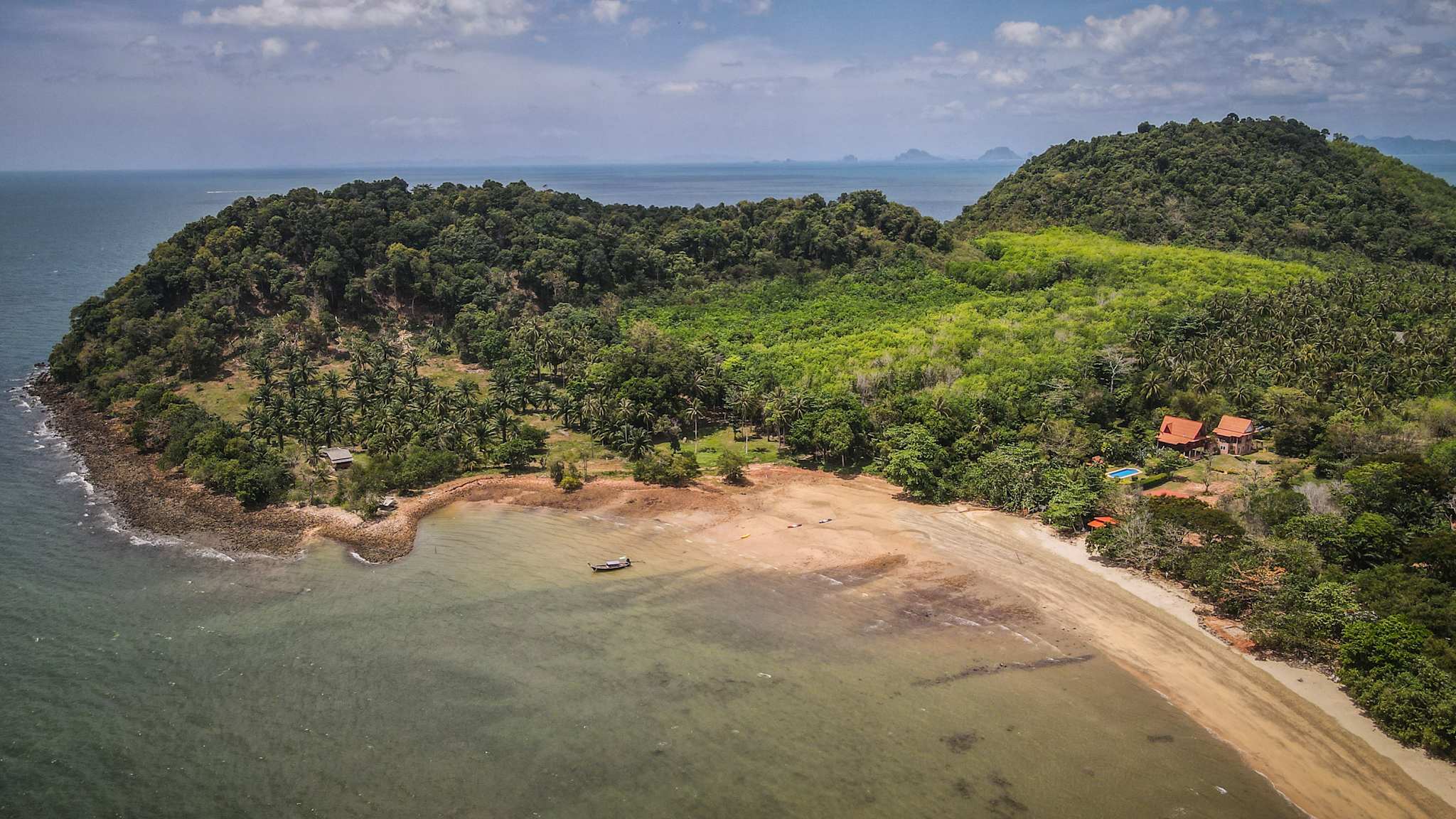 Blick von oben auf eine bewaldete Insel mit Strand und zwei Häusern