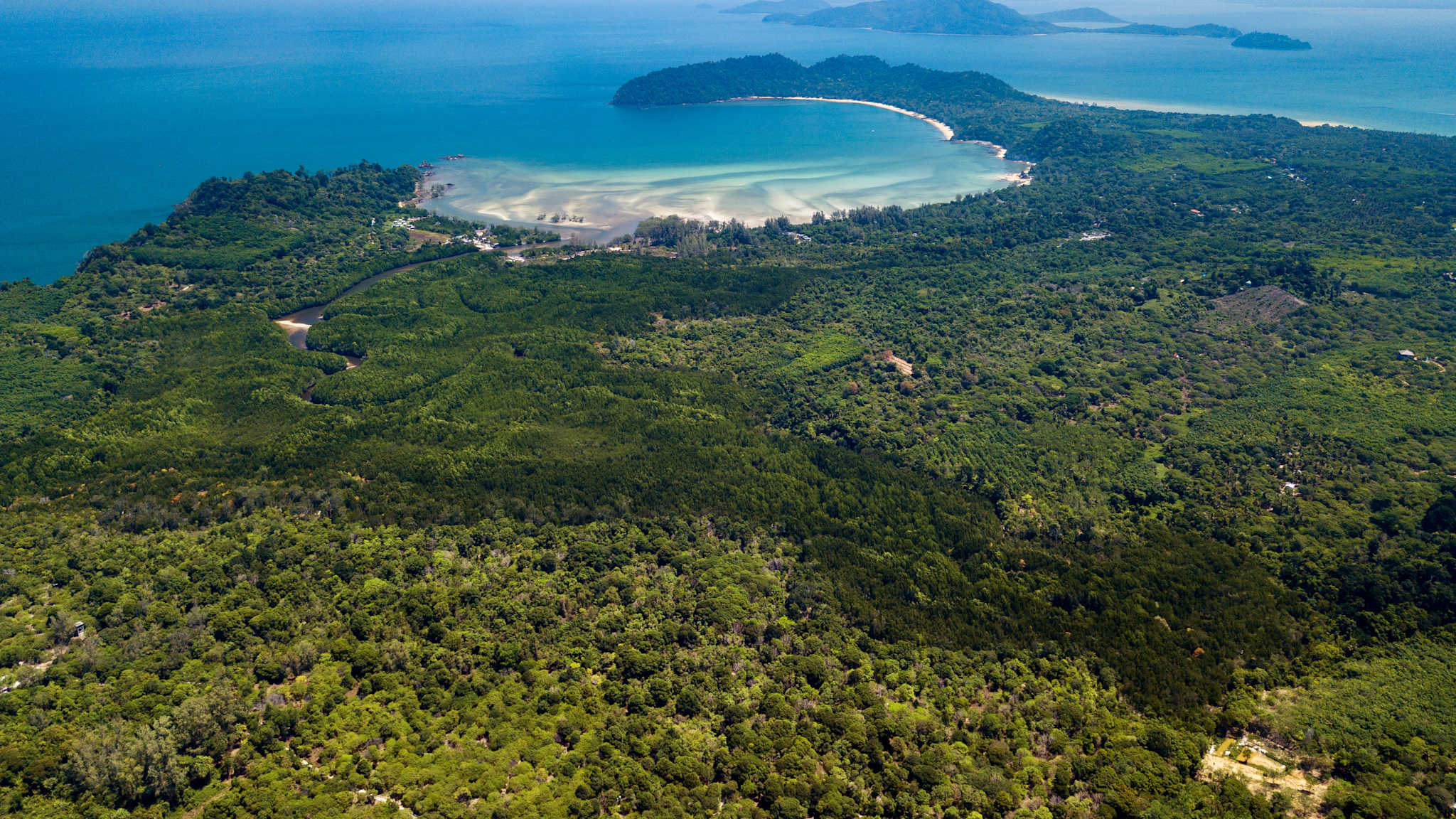 Blick von oben auf eine dicht bewaldete Insel mit einer Bucht und blauen Meer im hinteren Teil des Bildes