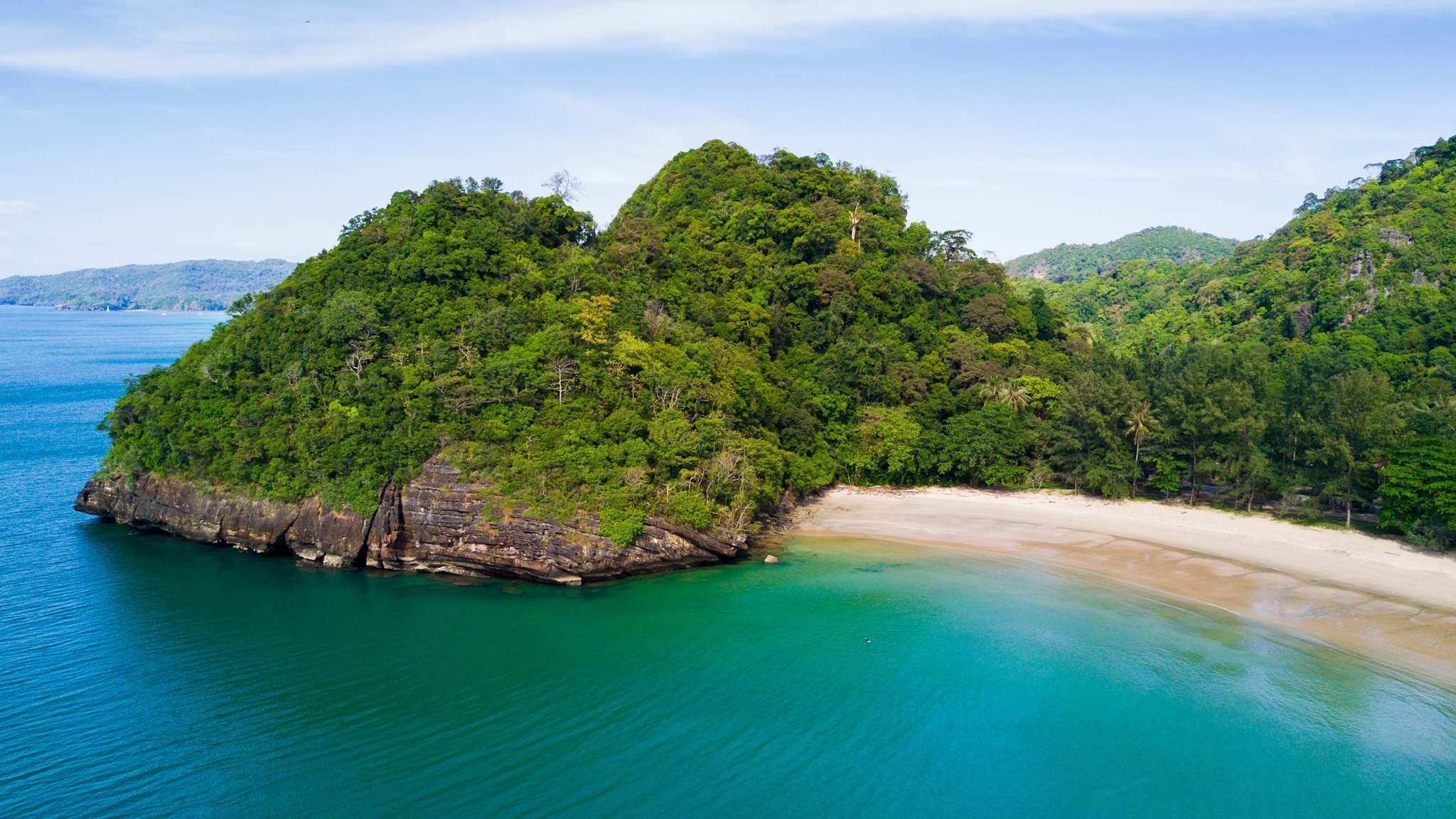 Blick aus der Luft auf eine dicht bewaldete Insel mit weißem Sandstrand