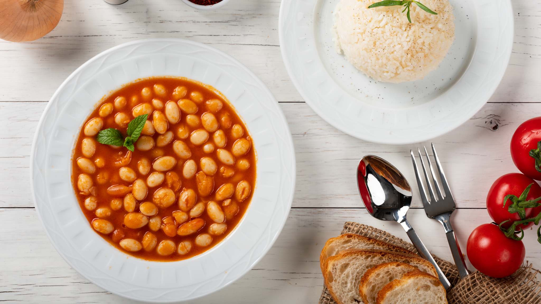 Teller mit Bohnen in Tomatensoße, daneben ein Teller mit Reis