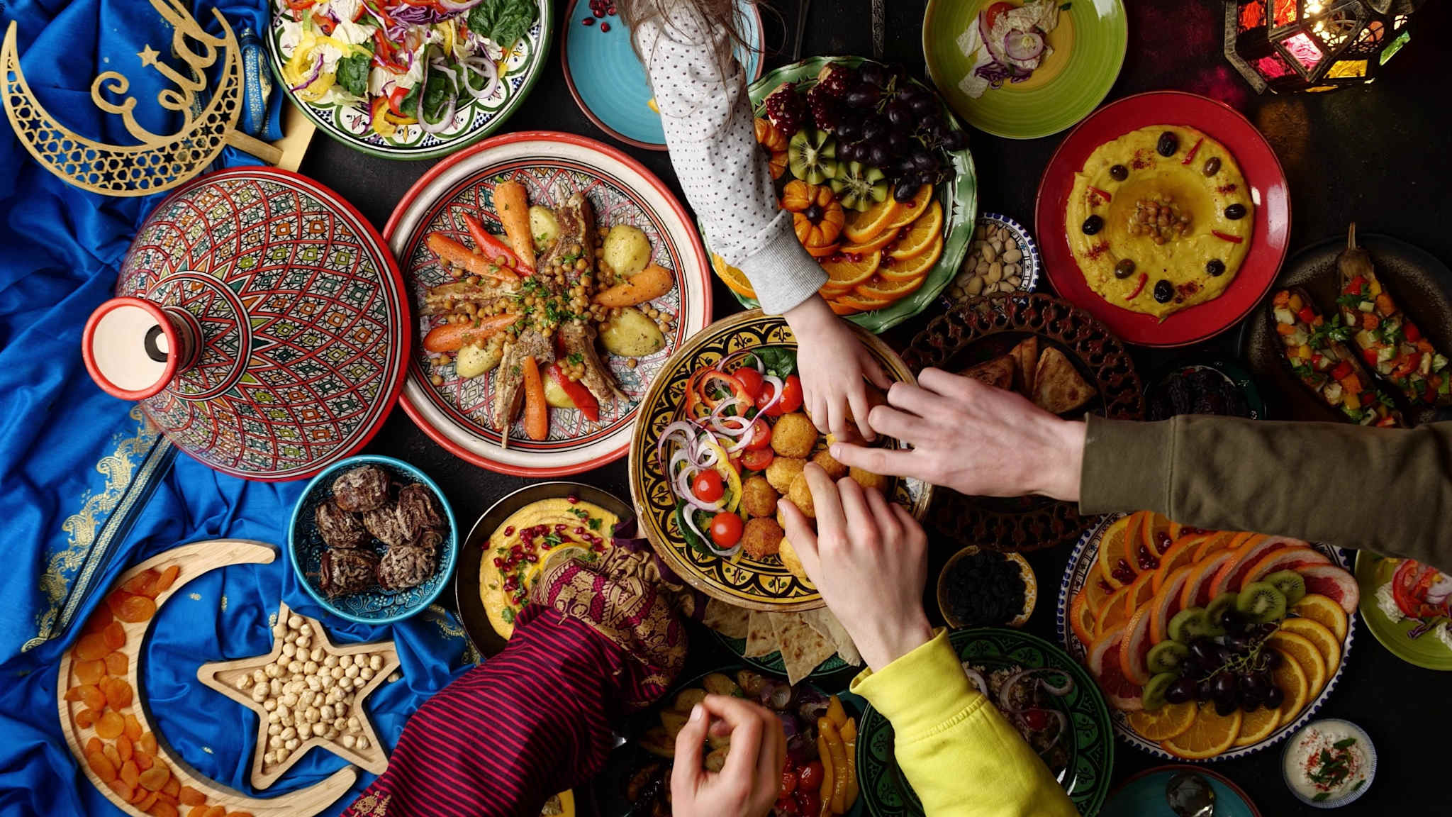 Blick von oben auf eine Vielzahl von Gerichten, mehrere Hände greifen nach Essen