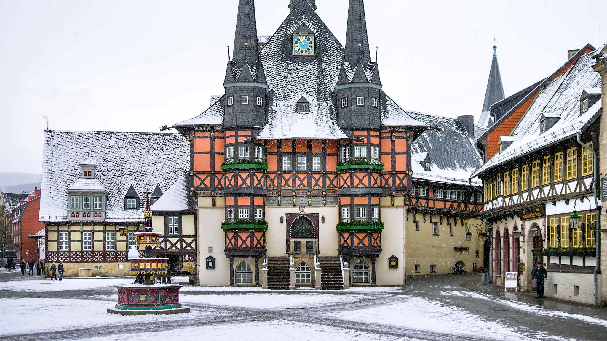 Fachwerkhaus mit zwei spitzen Türmchen vorne an verschneitem Marktplatz.