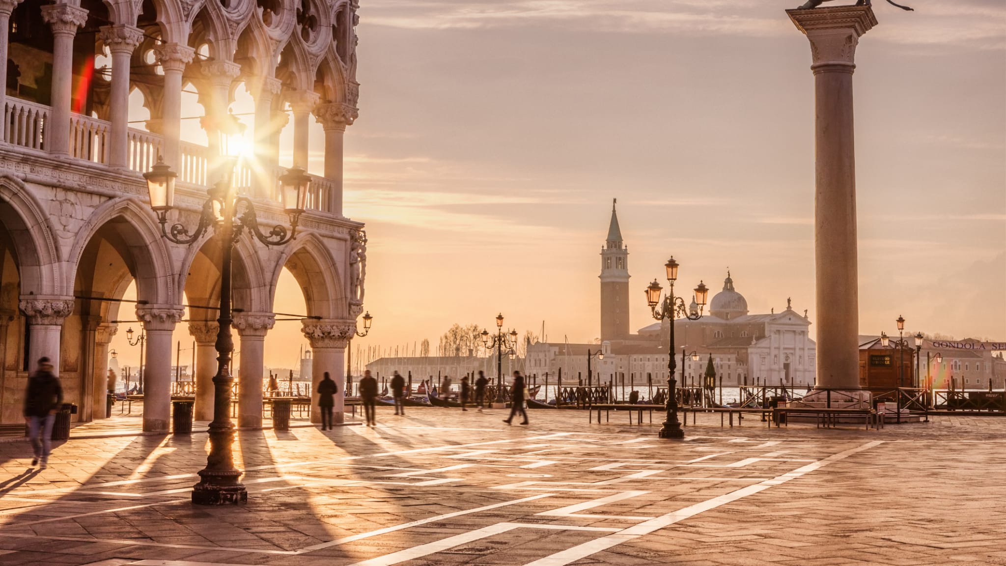 Menschen laufen bei tiefstehender Sonne über den St. Mark's Square, Venedig © iStock.com/tunart