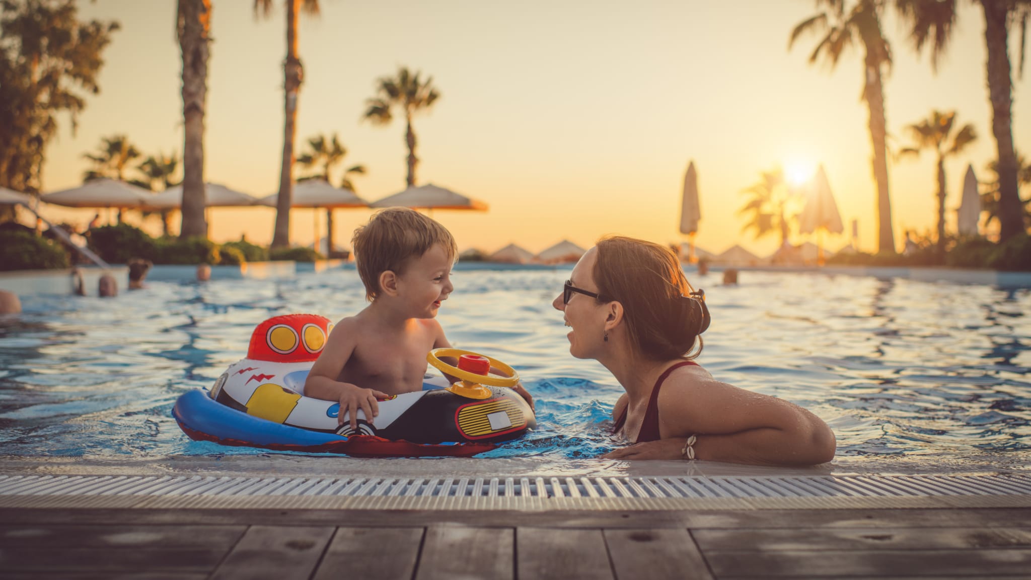 Mutter mit ihrem Kind im Pool beim Sonnenuntergang © iStock.com/ArtMarie
