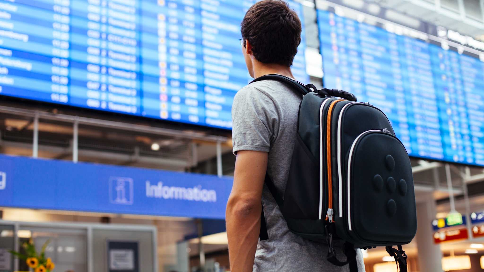Mann mit Rucksack blickt auf Anzeigetafel im Flughafen