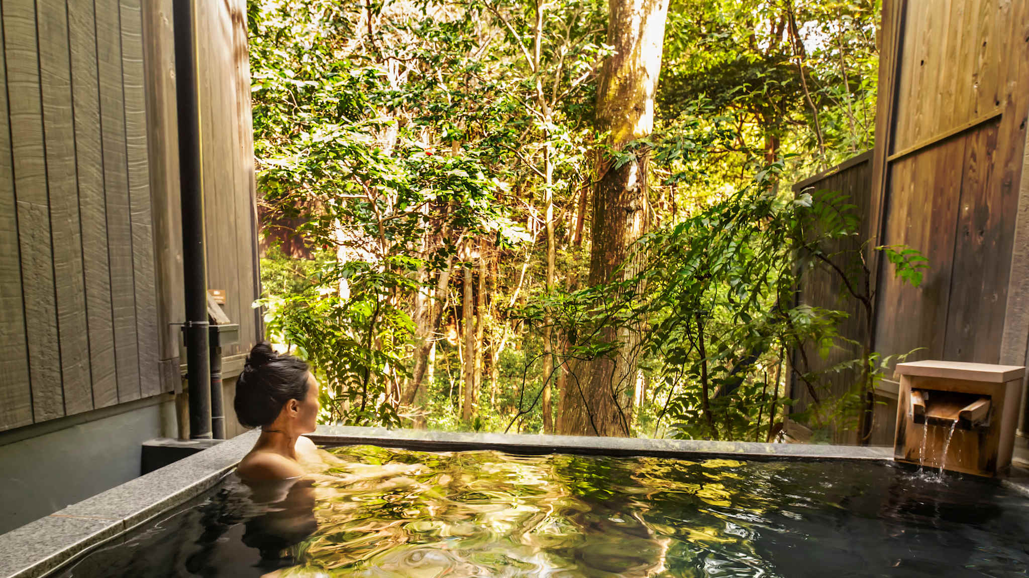 Frau baded in Onsen mit Wald im Hintergrund
