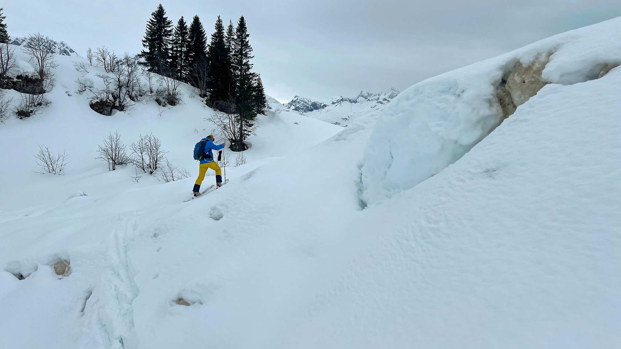 Ein Skitourengeher bahnt sich seinen Weg durch die verschneite Landschaft im Vorarlberger Bergparadies, nahe der beeindruckenden Gipfelkulisse.