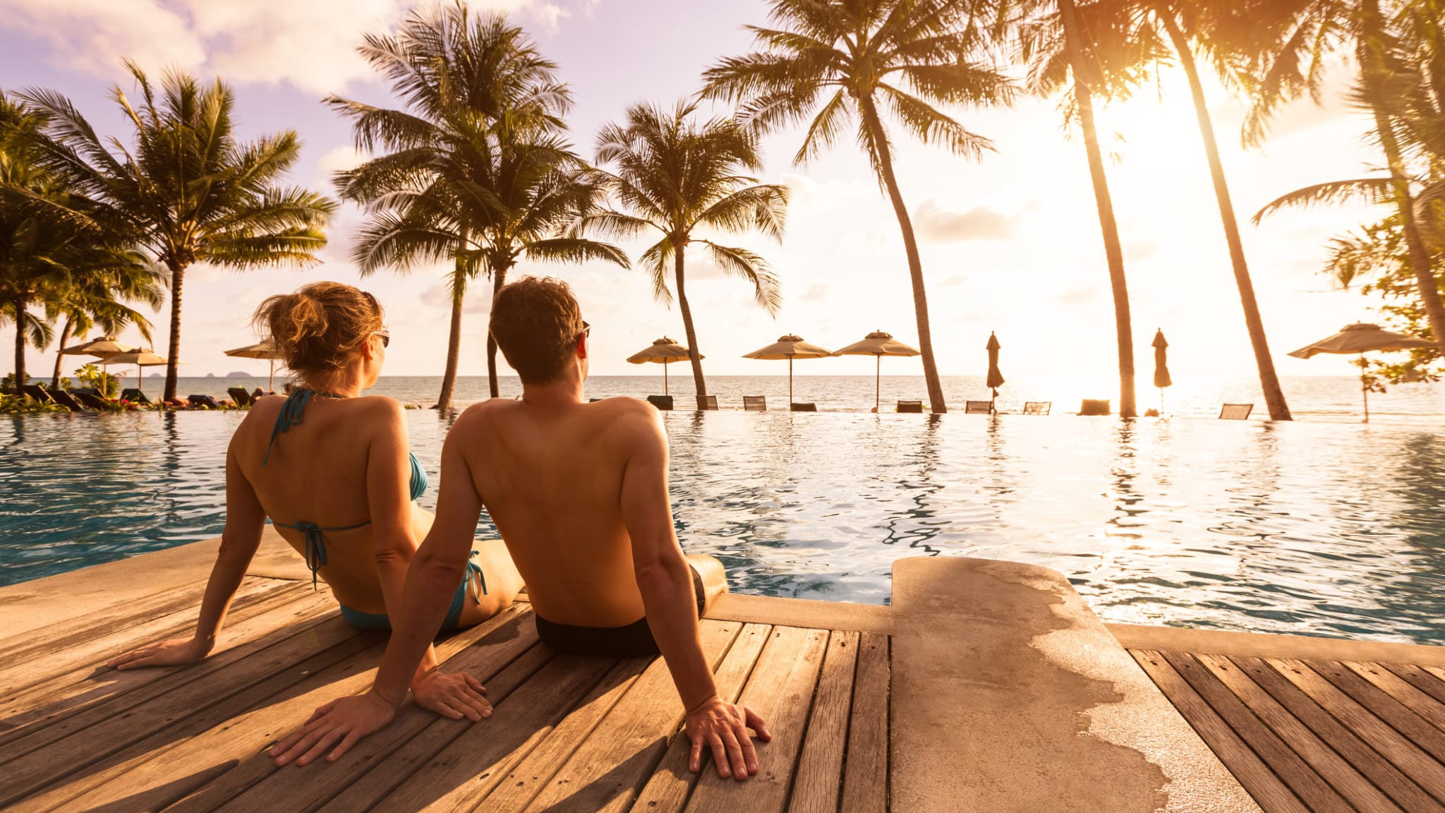 Ein Paar genießt ihren Strandurlaub in einem tropischen Resort mit Pool bei Sonnenuntergang ©NicoElNino/iStock
