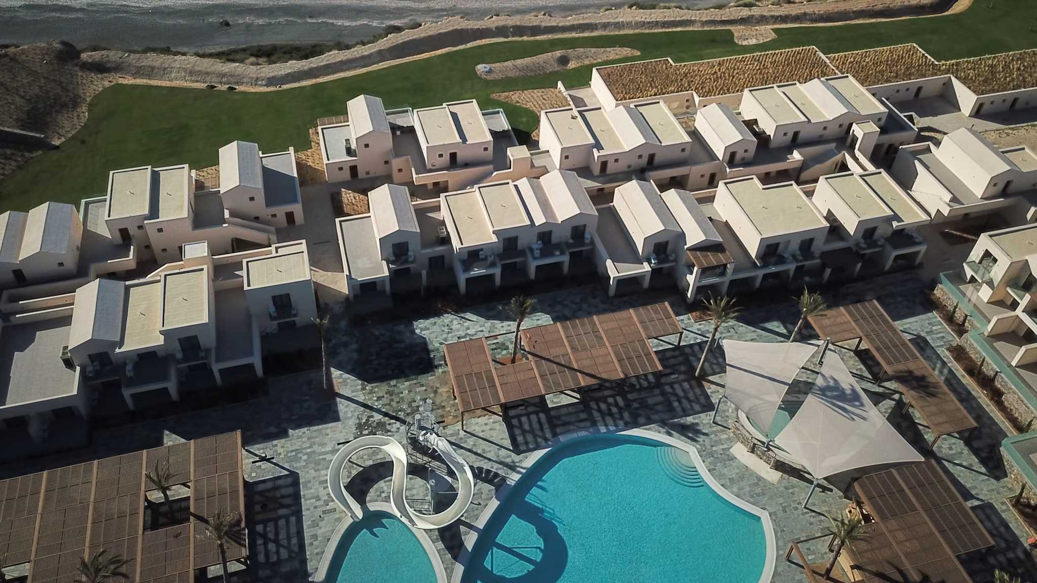 Luftaufnahme einer Hotelanlage mit Bungalows zwischen einem Pool und dem Meer