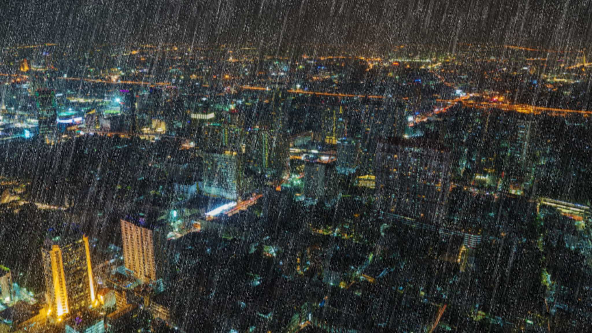 Blick aus Vogelperspektive auf Bangkok nachts bei fallendem Regen.