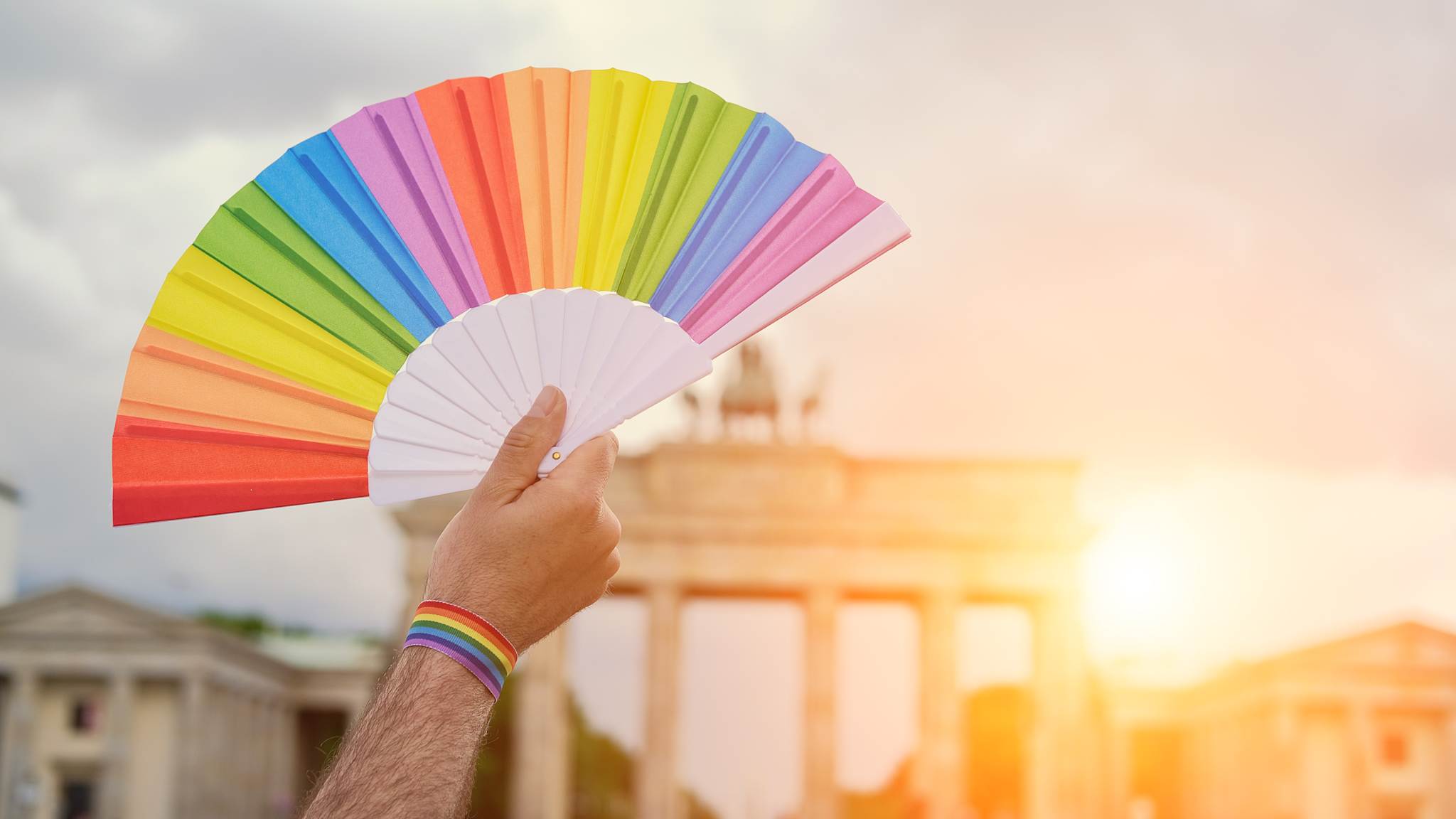 Eine Hand hält einen Regenbogenfächer hoch vor dem Brandenburger Tor in Berlin