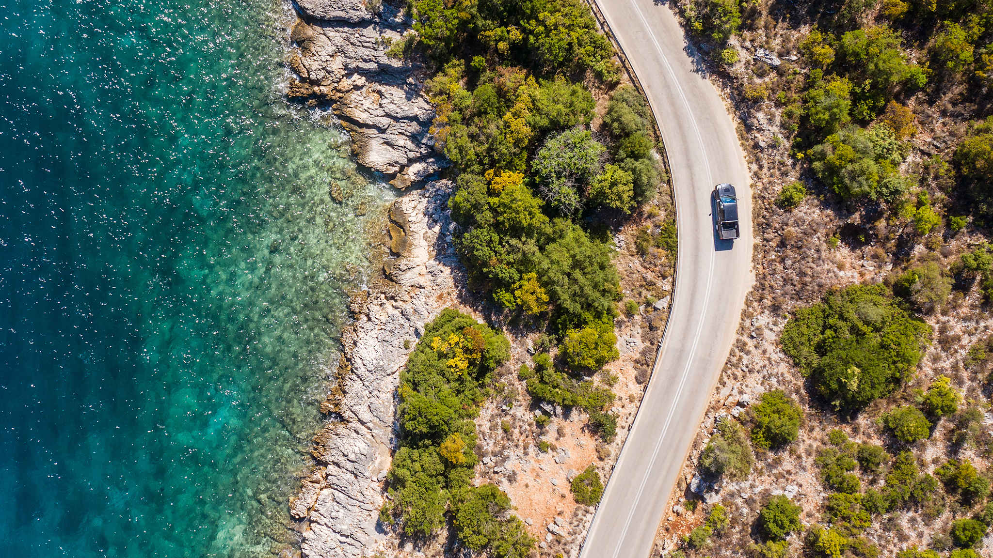 Blick von oben auf ein Auto auf einer Straße am Meer