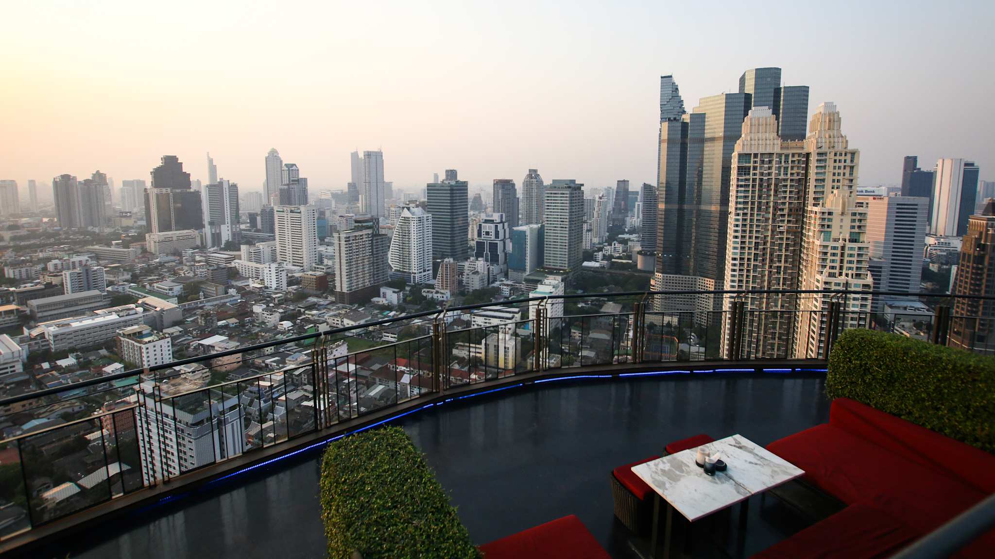 Ausblick von einer Rooftop-Bar mit rot bezogenen Sofas auf die Hochhäuser von Bangkok.