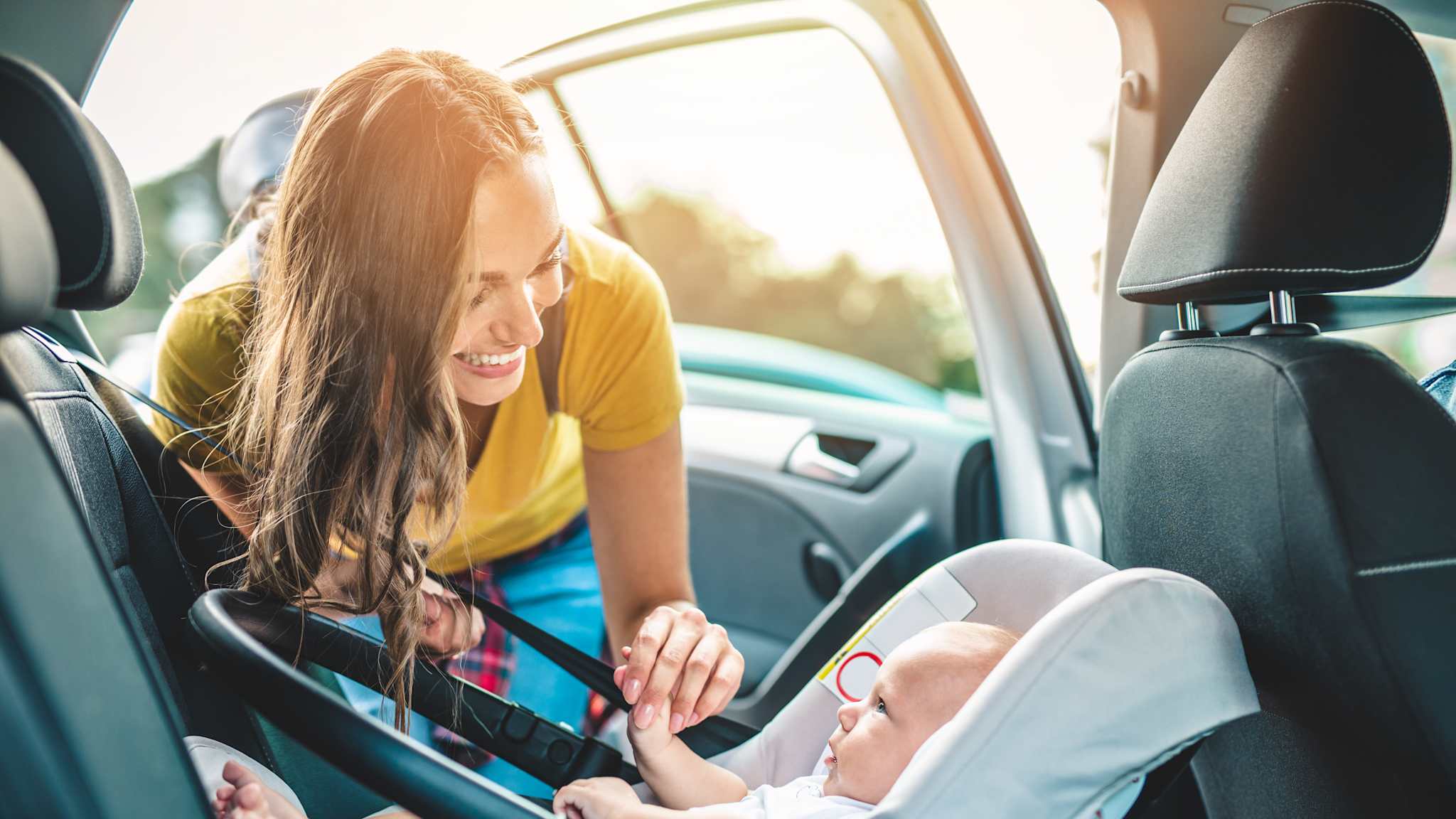 Eine Mutter befestigt ihr Kleinkind im rückwärtsgerichteten Sitz auf dem Rücksitz.