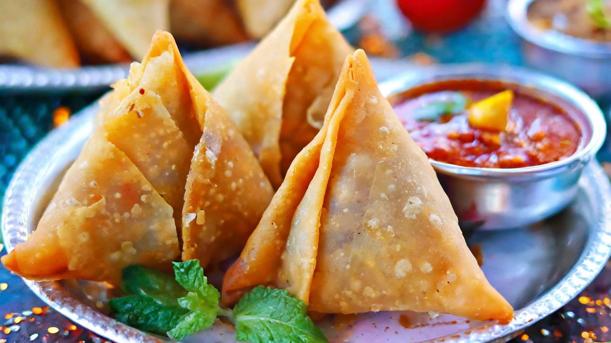 Mehrere Samosas liegen auf einem silbernen Teller mit einer kleinen Soßenschale.