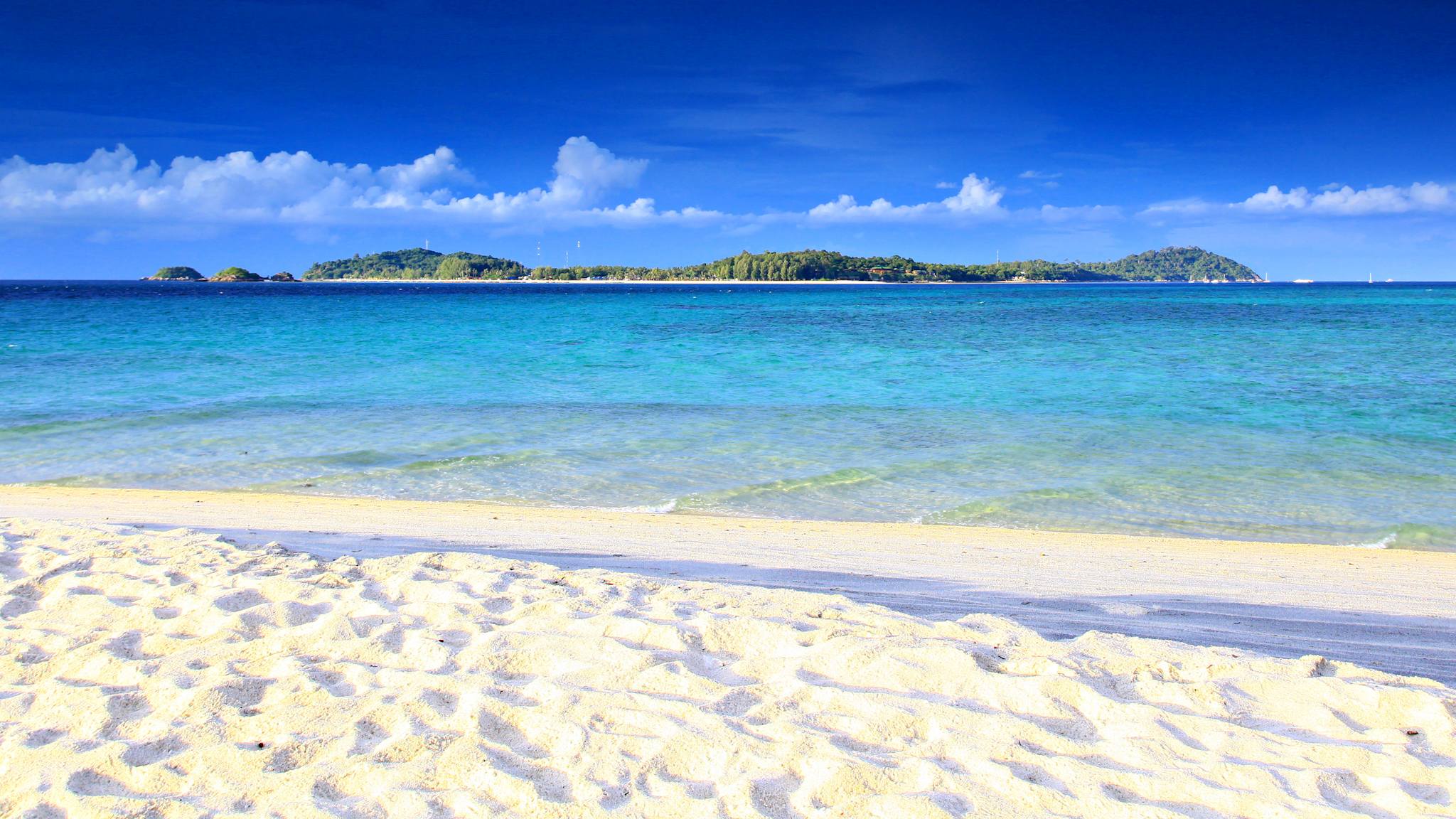 Blick auf einen weißen Sandstrand am Meer mit einer Insel im Hintergrund