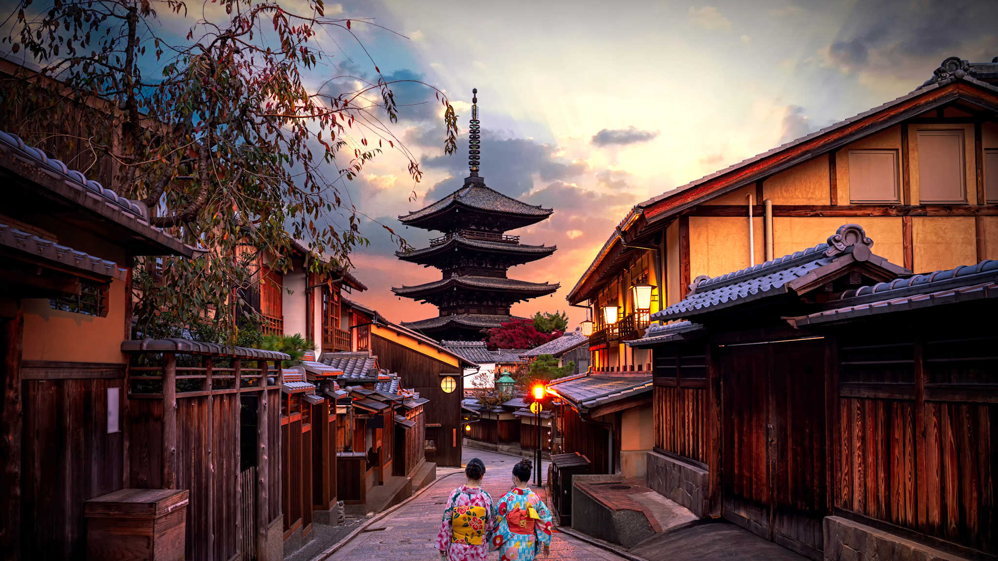 Zwei Frauen laufen eine Gasse in Kyoto entlang, mit Blick auf einen Tempel
