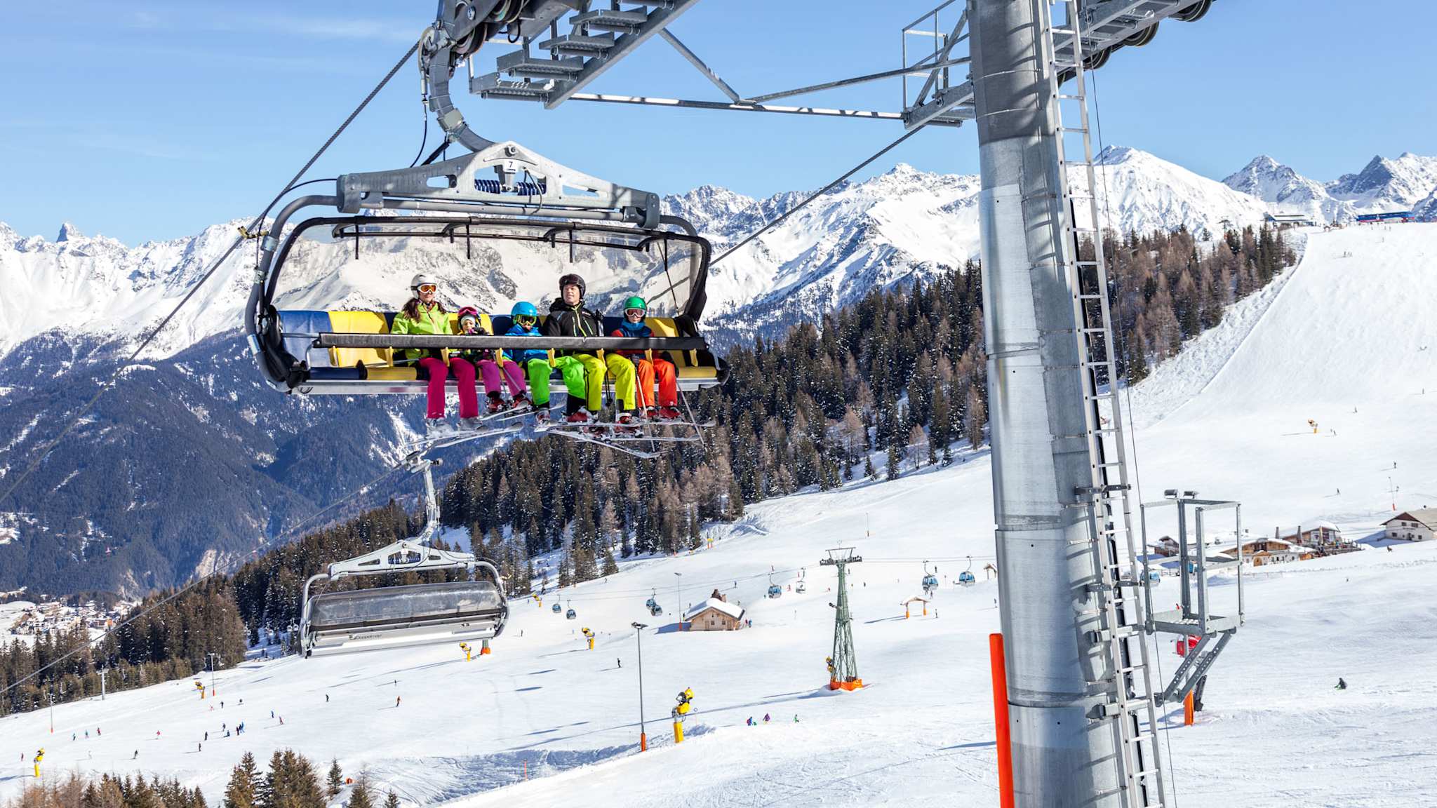 Familien und Kinder sitzen gemeinsam im Sessellift in Serfaus-Fiss-Ladis, Tirol, mit Blick auf verschneite Pisten und Berge.