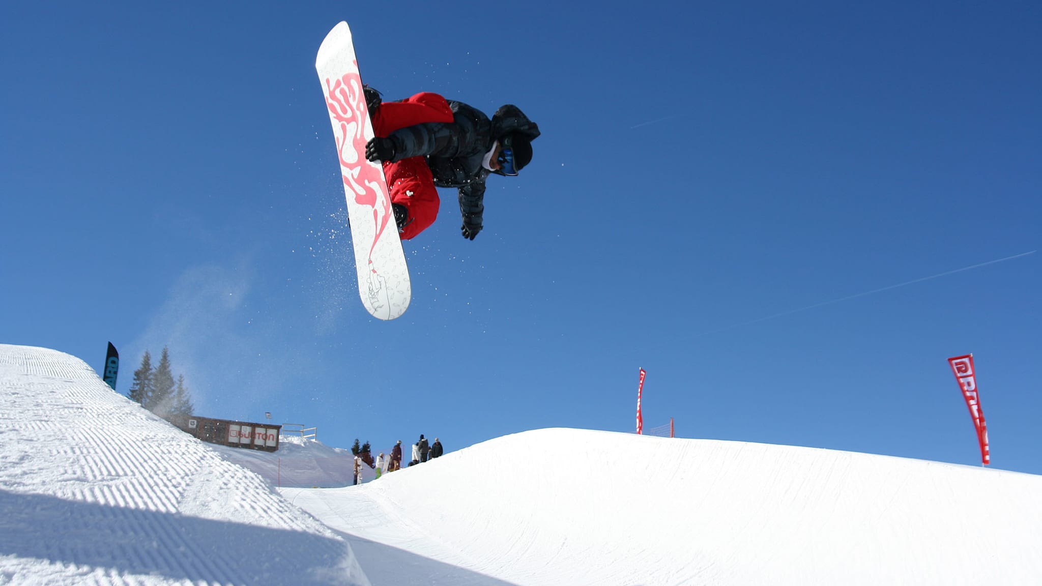 Snowboarder in der Luft beim Trick über einen Kicker im Funpark, blauer Himmel im Hintergrund, Avoriaz, Schweiz.