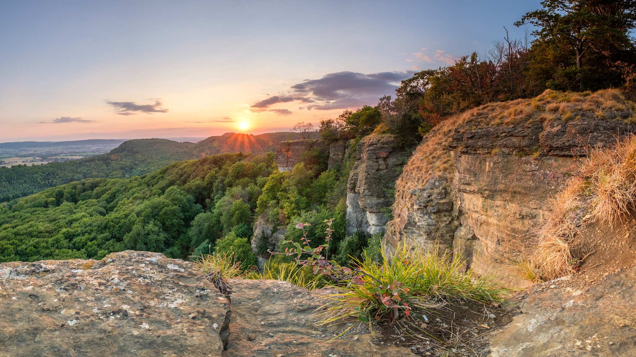 Die Ith-Klippen im Weserbergland bei Sonnenuntergang, mit einem weiten Blick über die grüne Landschaft und die markanten Felsformationen.