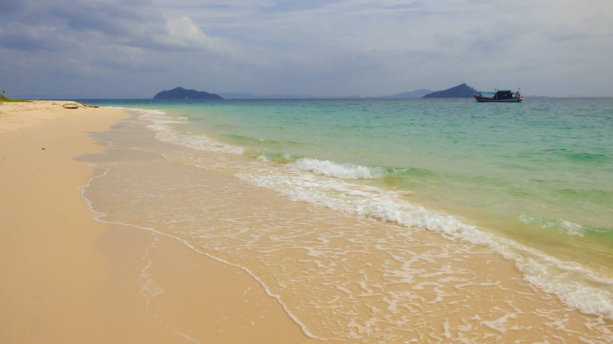 Weißer Sandstrand am Meer mit kleinem Boot im Hintergrund