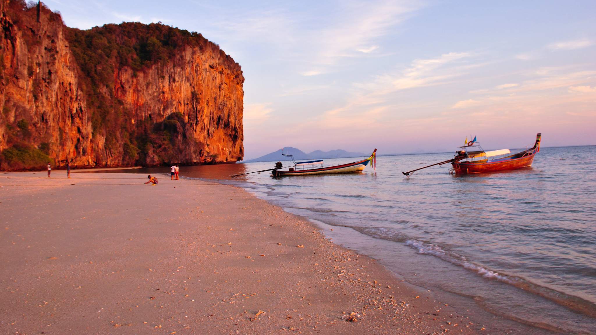 Strand bei Morgenlicht mit zwei kleinen Booten im Wasser und einer Felsstruktur im Hintergrund