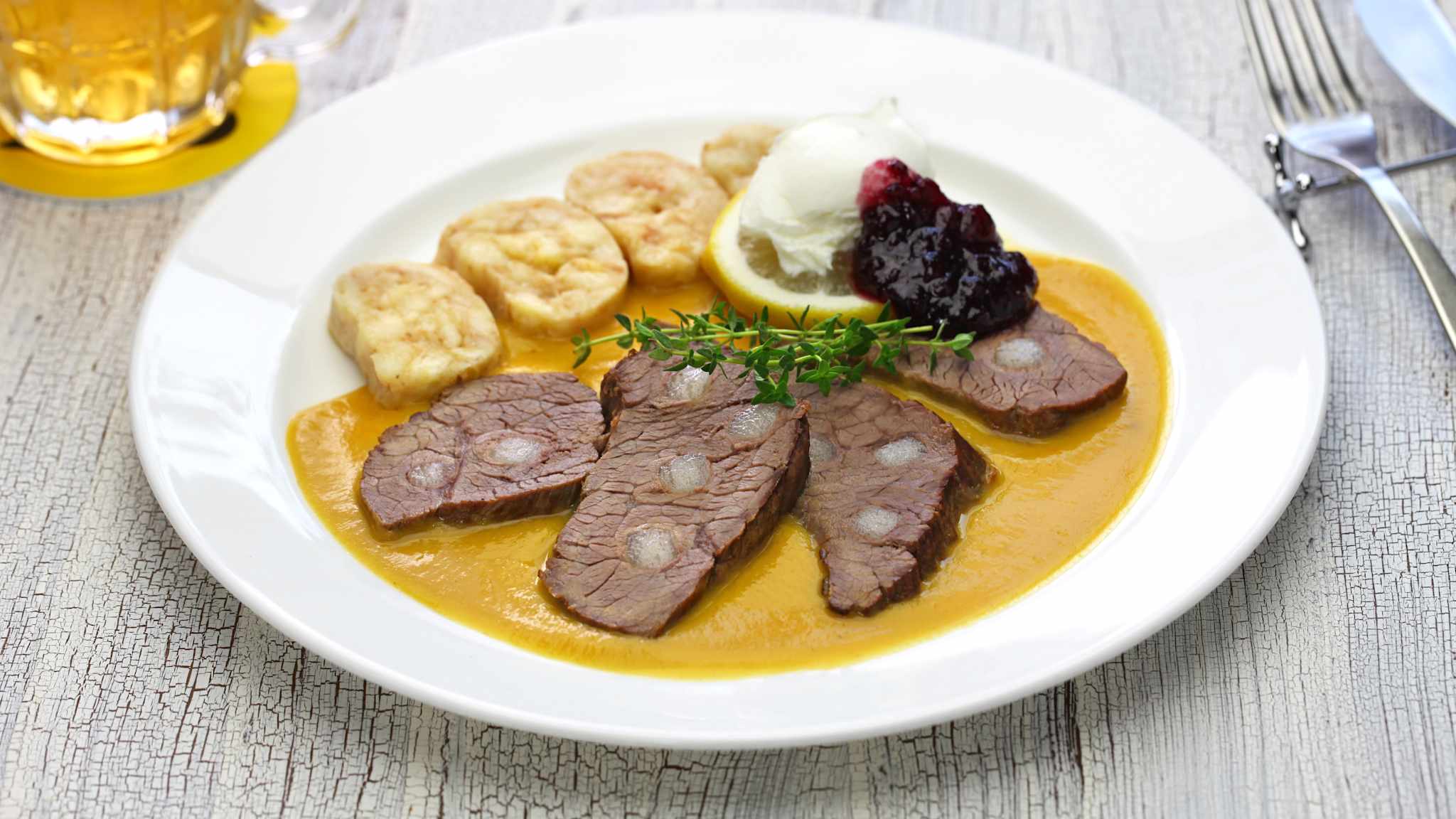 Tschechisches Gericht mit Rinderlende in Wurzelgemüse-Sahne-Soße mit Semmelknödel, einer Zitronenscheibe und Preiselbeerkompott.