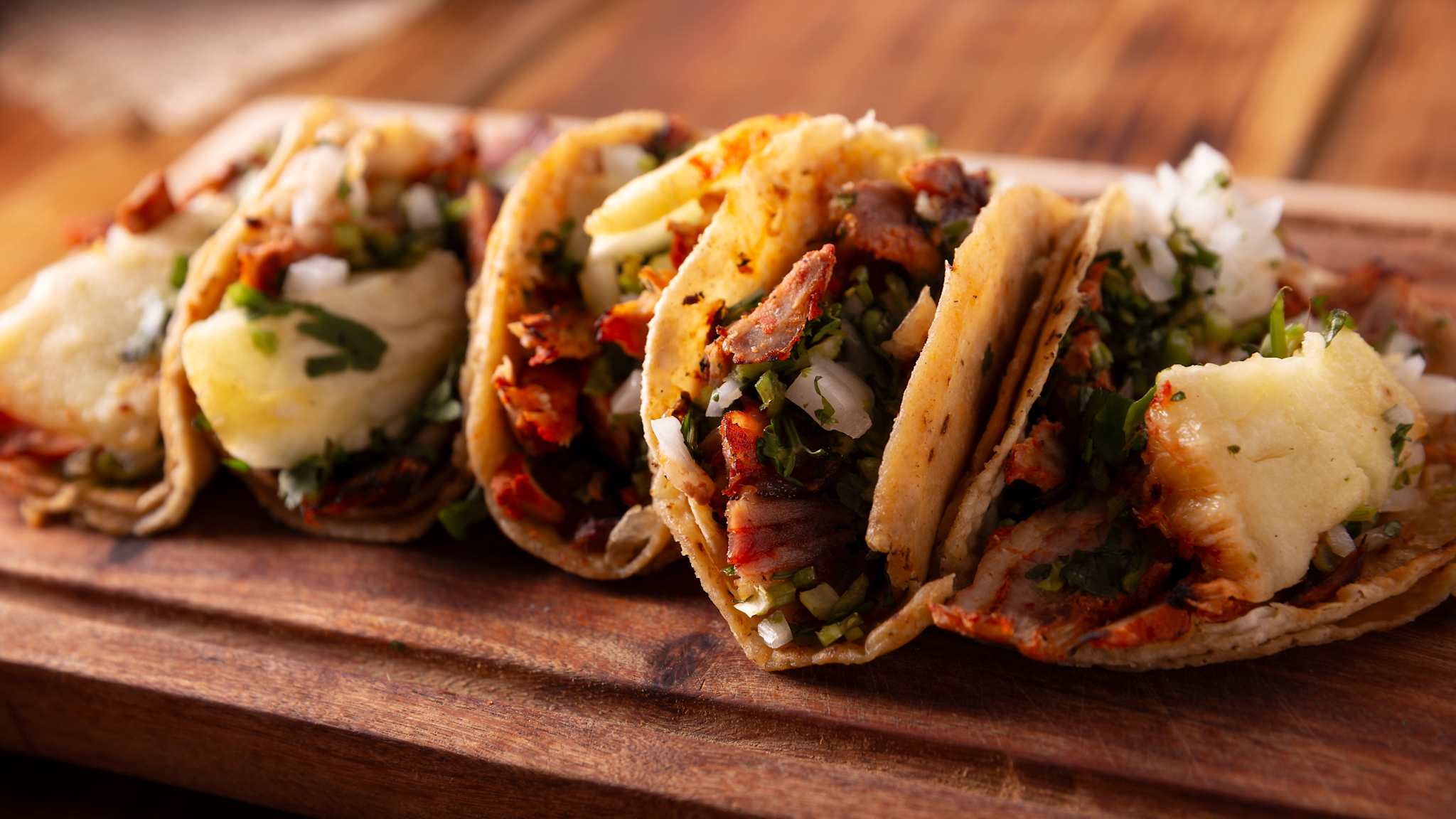 Holzbrett mit mehreren Tacos, gefüllt mit Fleisch