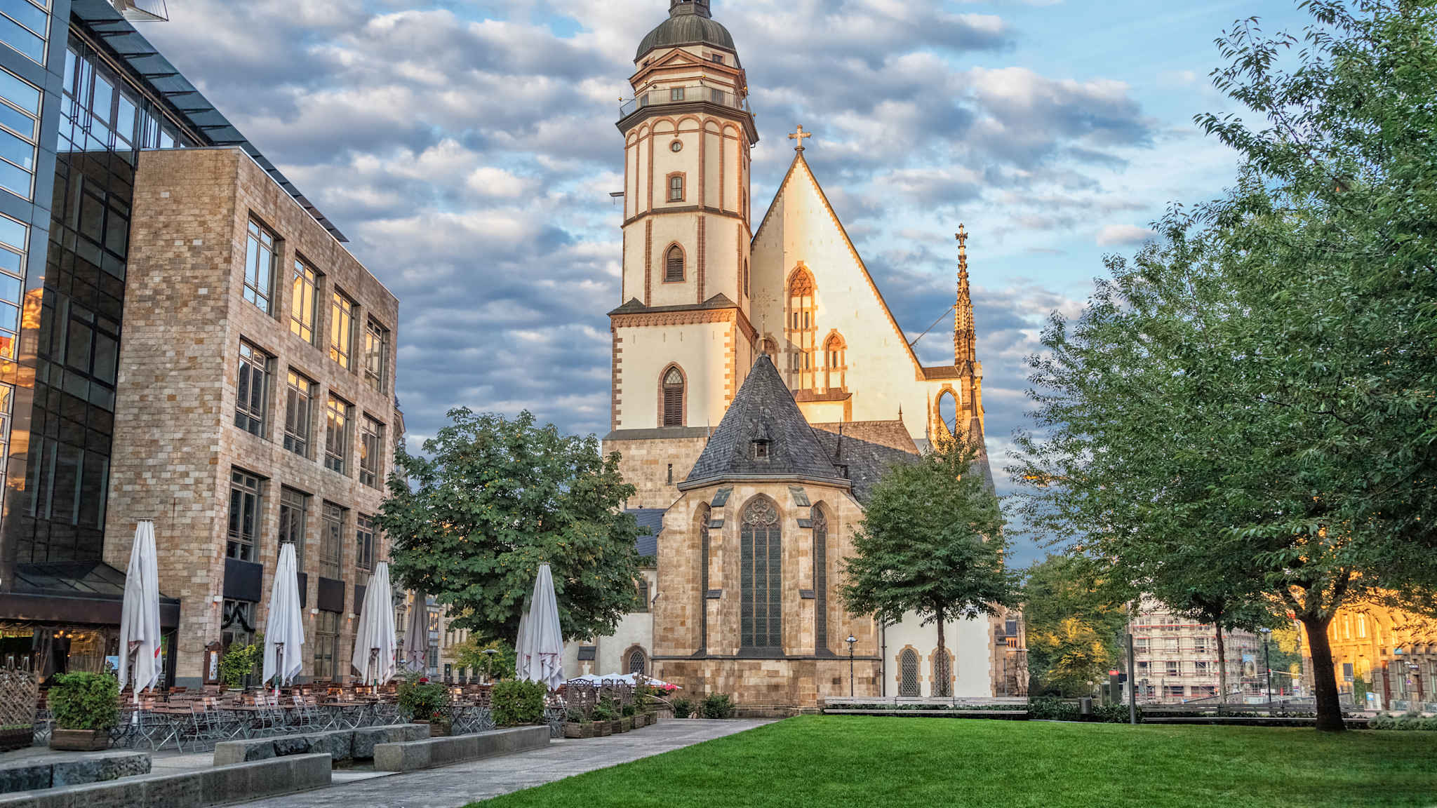 Blick auf die Thomaskirche in Leipzig mit einer Wiese und einem Cafe davor.