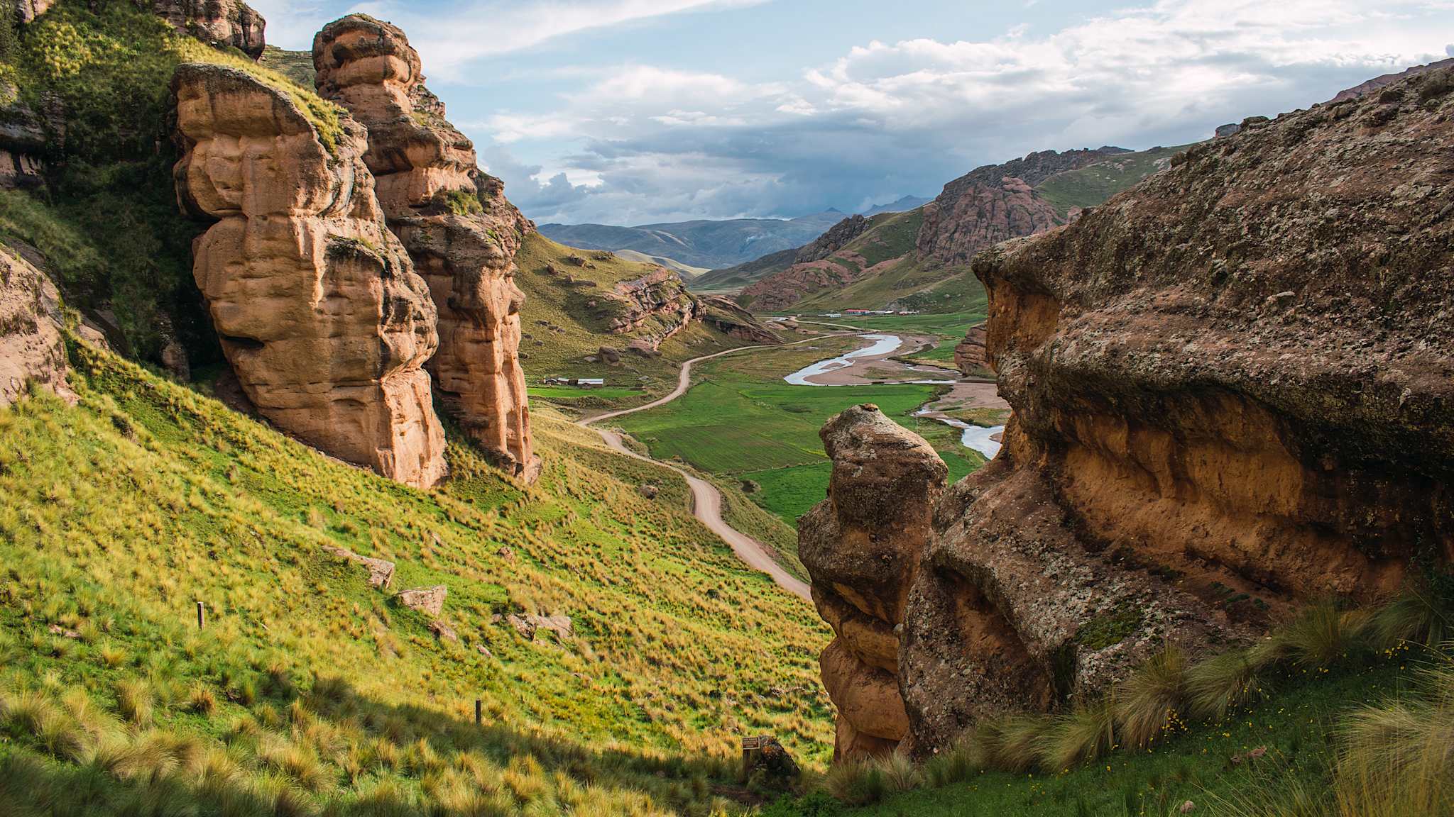 Blick aus Felsen an Berghang auf Tal mit Pfad und Bach zwischen steinigem Tinajani Gebirge in Perus Anden.