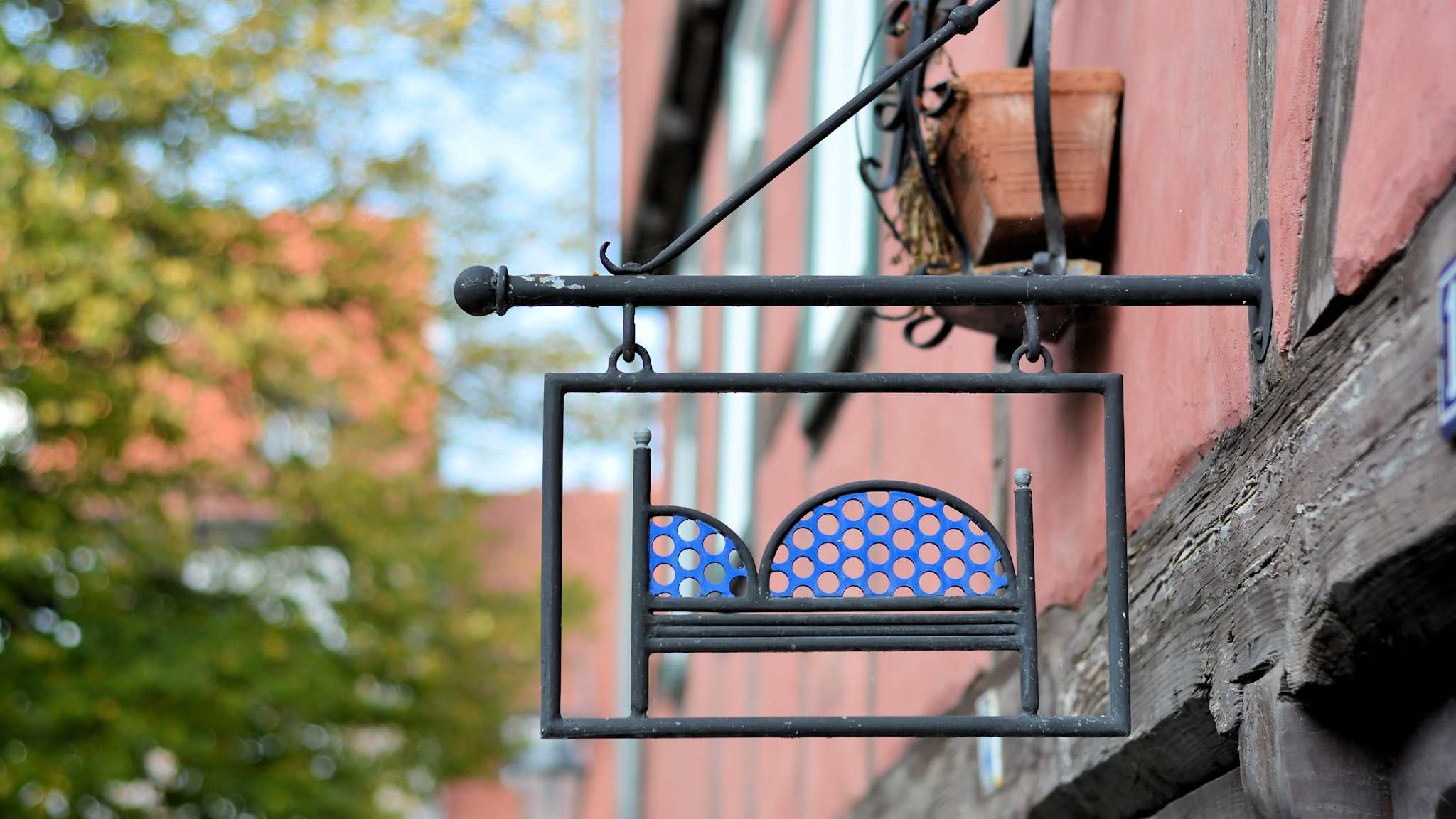 Ein Metallschild mit einem darauf abgebildeten Bett hängt an einer Häuserwand.