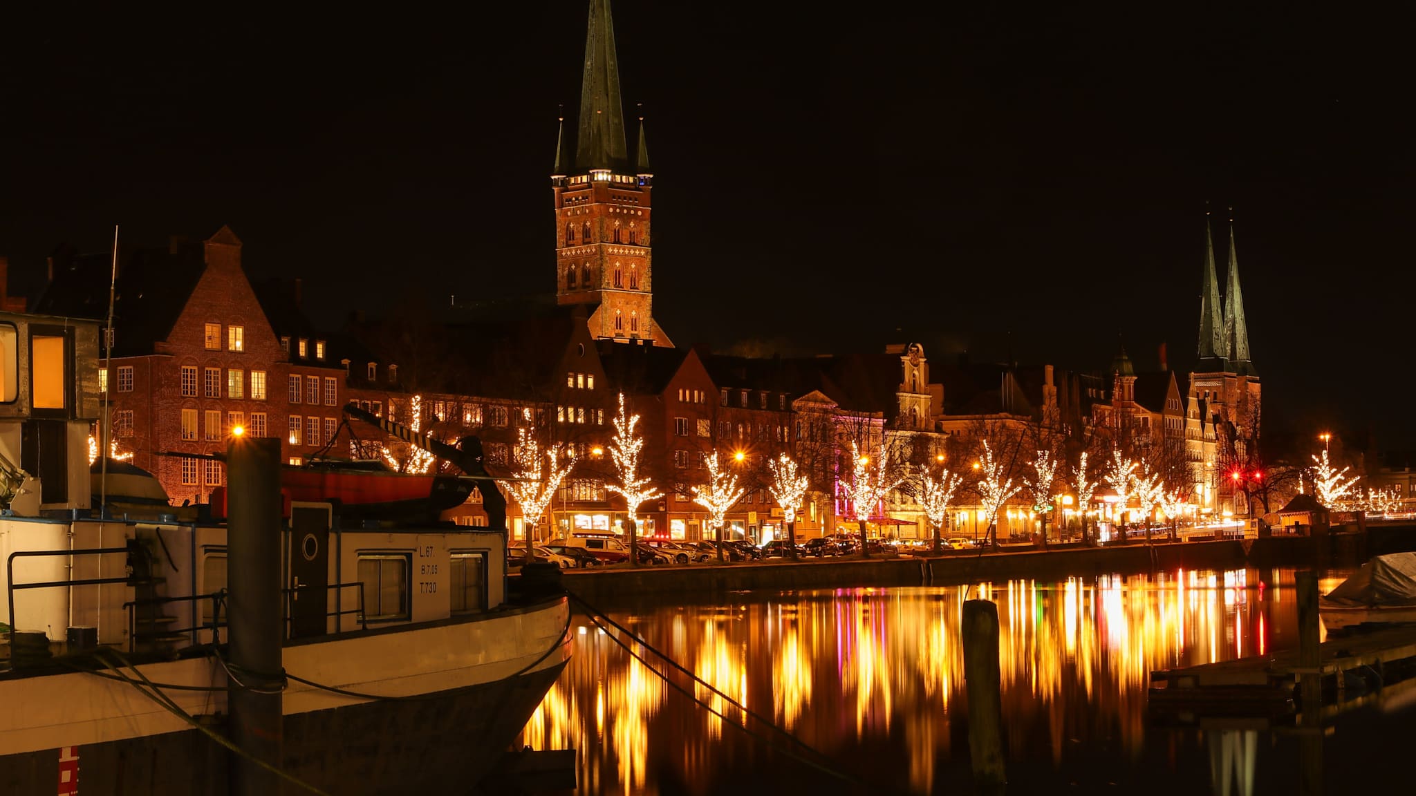 Mit Lichterketten erleuchtete Bäume vor Altstadthäusern an der Trave in Lübeck nachts.