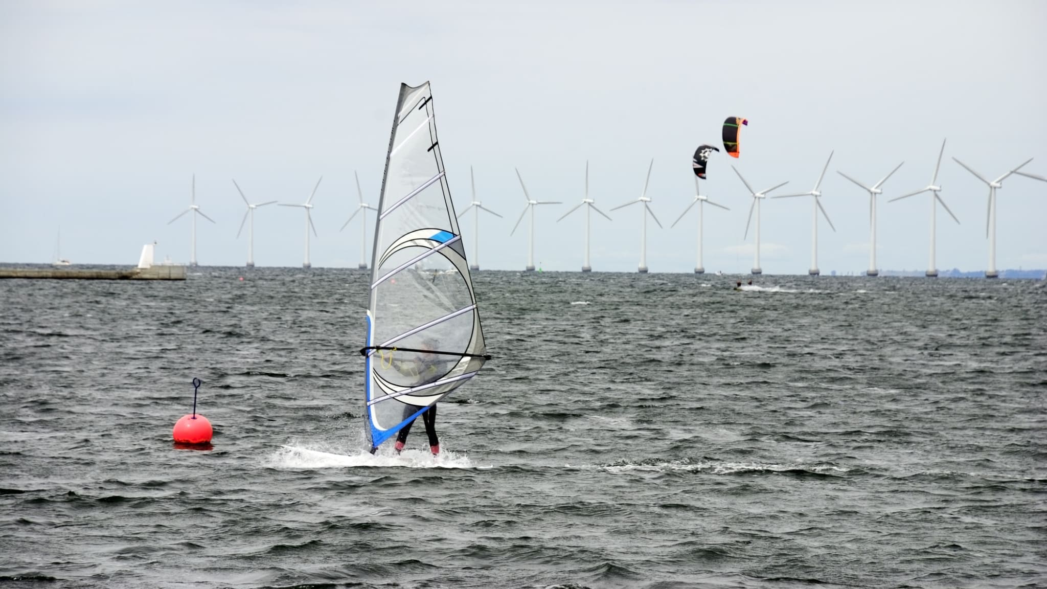 Windsurfer und Kitesurfer im Meer mit Windturbinen im Hintergrund © iStock.com/monap
