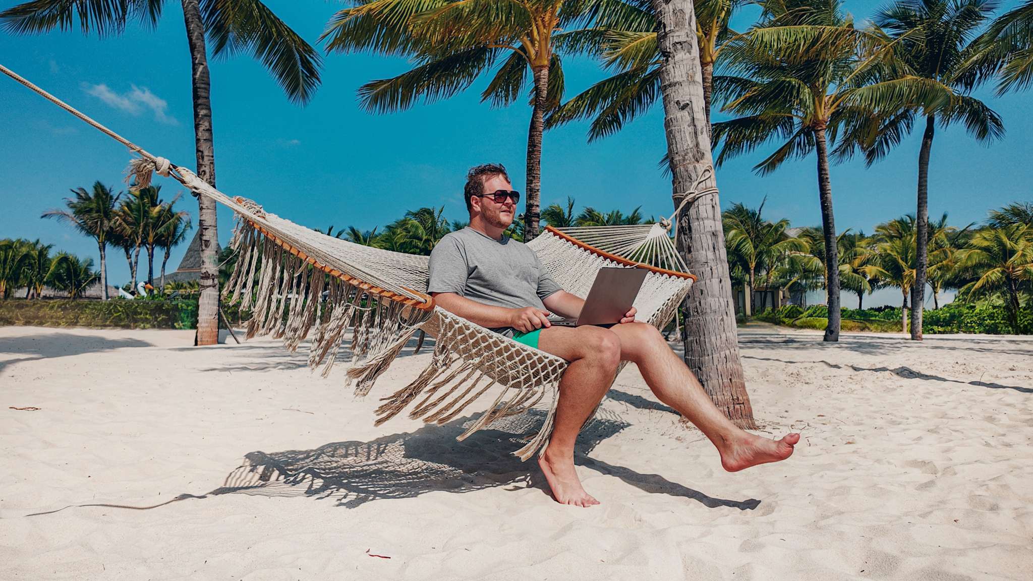 Mann sitzt am Strand in einer Hängematte mit einem Laptop auf dem Schoß