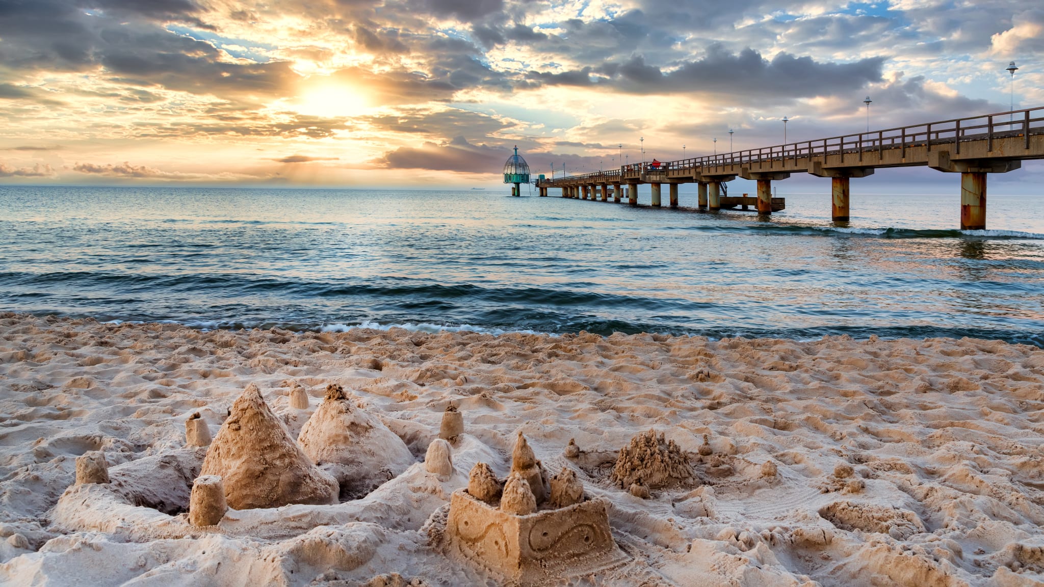Strand mit Sandburg und einem langen Steg.