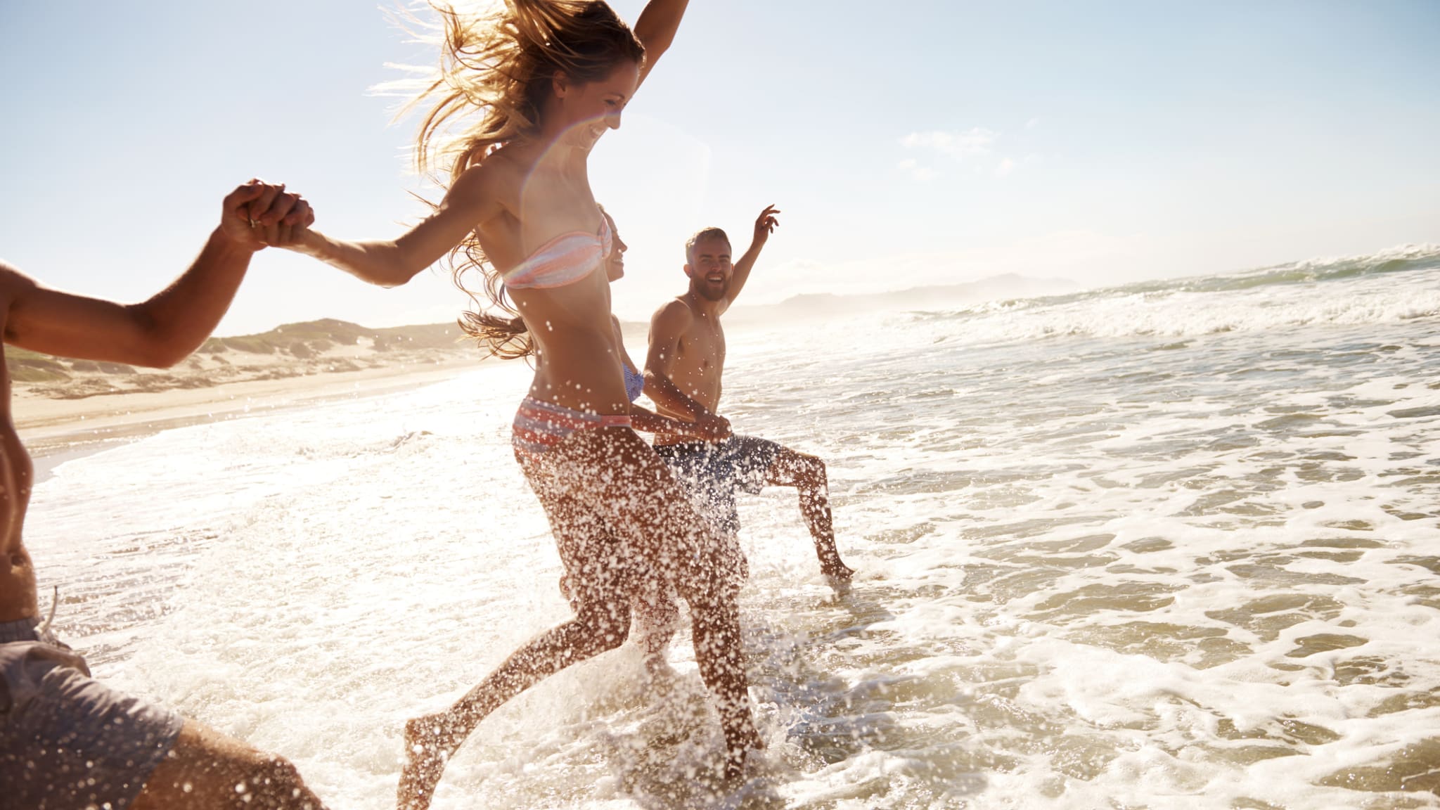 Zwei junge Paare, die am Strand durch das Wasser rennen © iStock.com/pixdeluxe