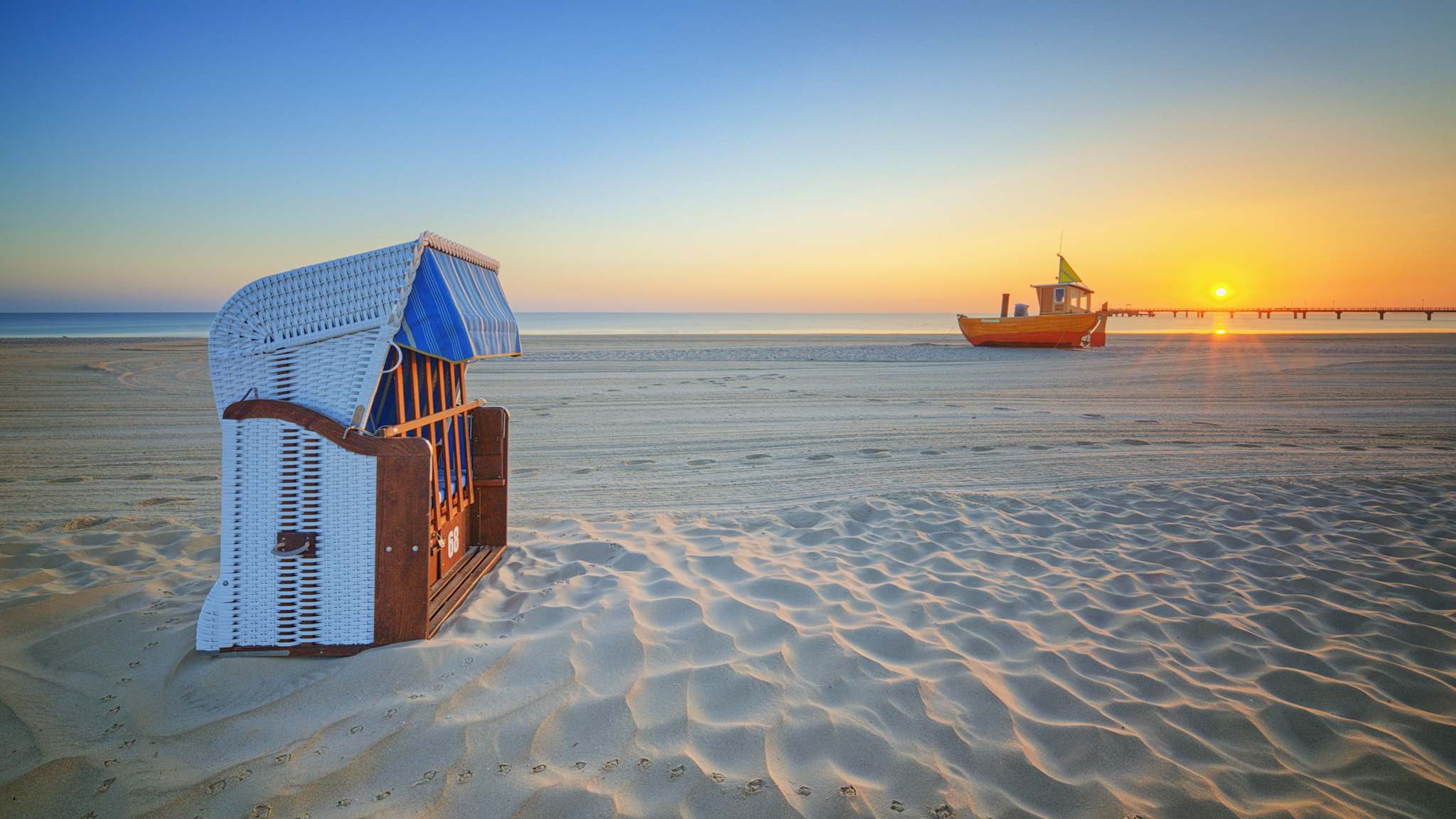 Ein Strandkorb und ein Fischerboot liegen auf einem Strand.