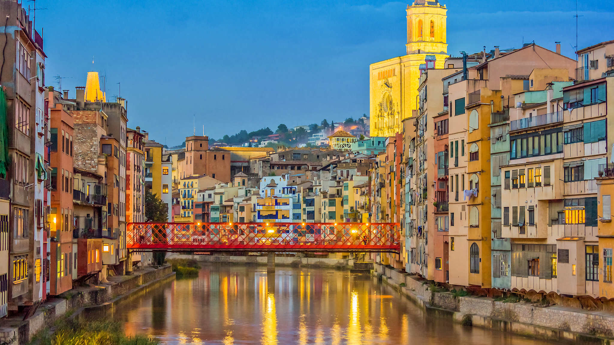 Eine Fußgängerbrücke überspannt einen Fluss in einer Stadt zwischen dicht bebauten Häuserreihen.
