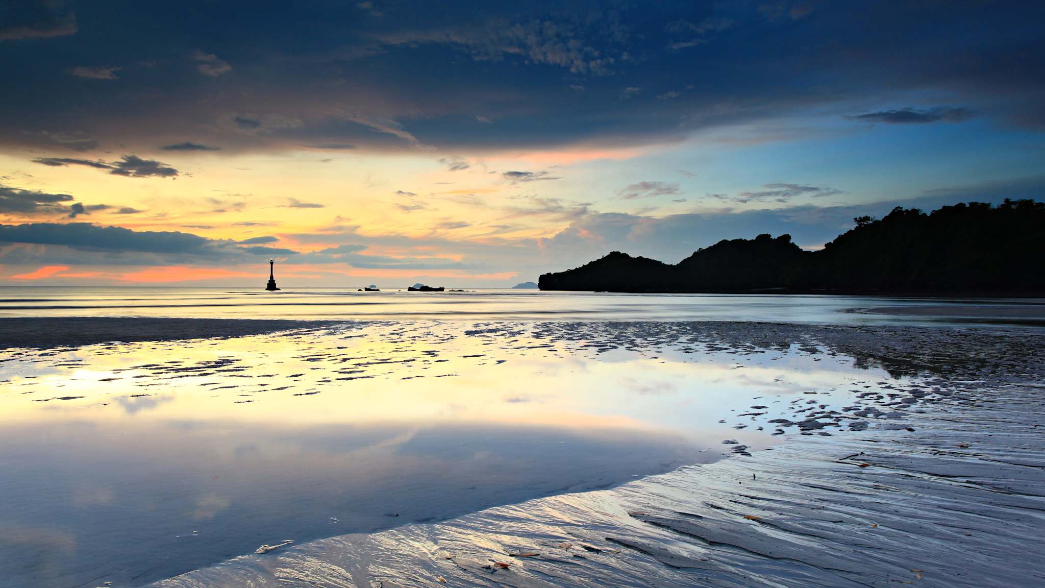 Sonnenuntergang an einem Strand. Das Wasser reflektiert die Wolken am Himmel.