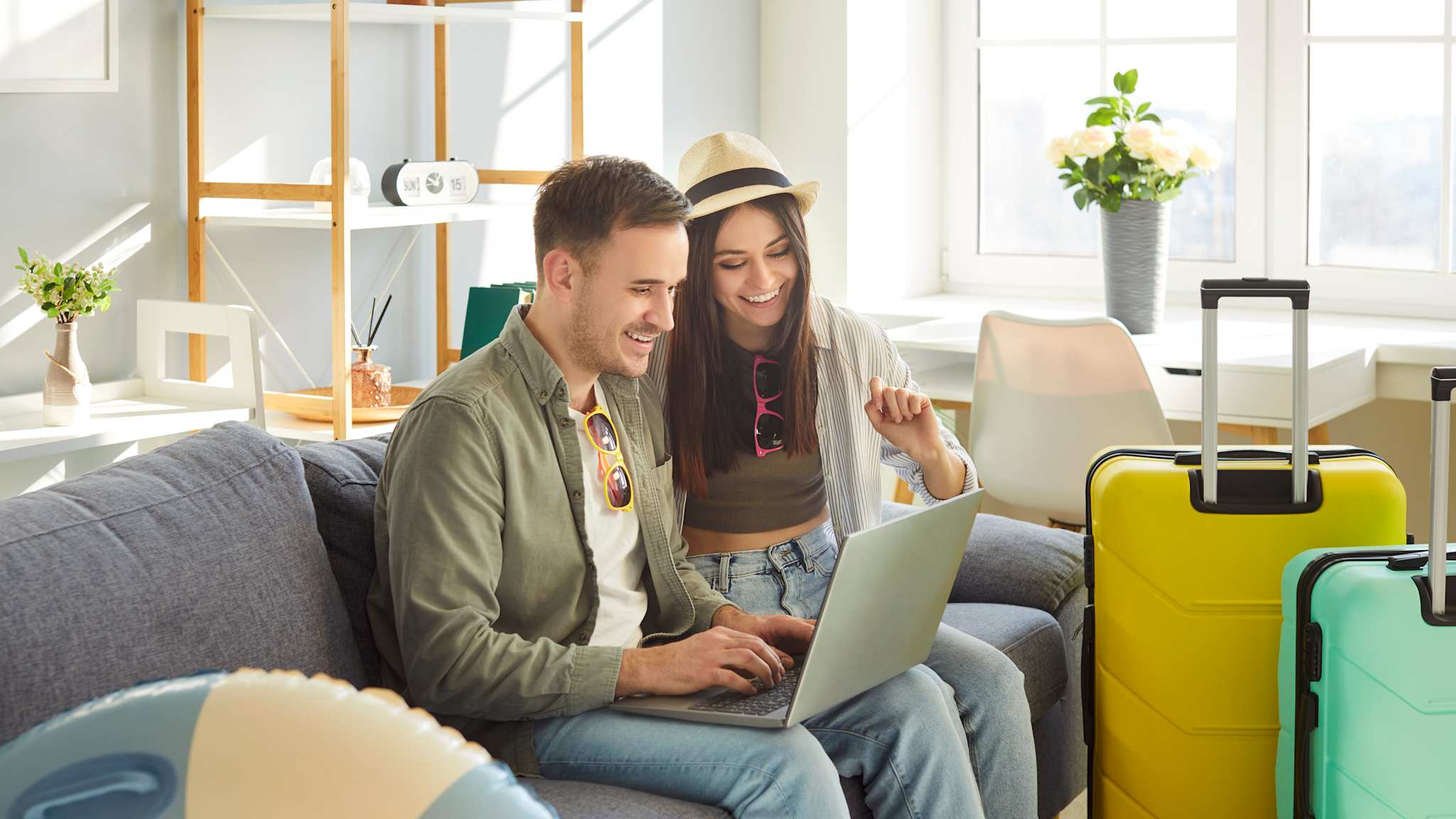 Ein Paar sitzt auf einer Couch und benutzt den Laptop. Im Raum verteilt stehen Koffer und ein Schwimmreifen.