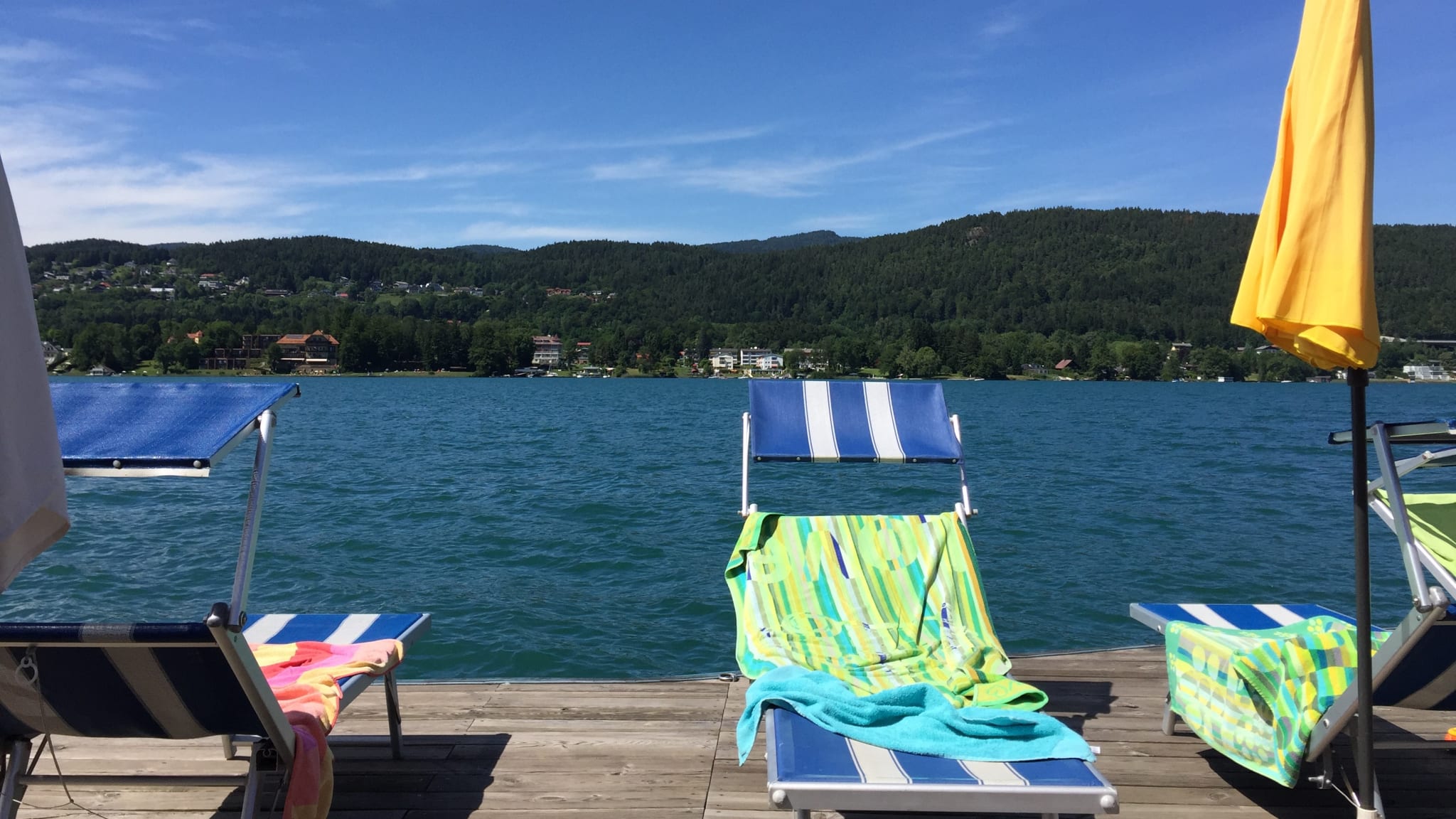 Blick vom Steg mit Liegen und Badehandtüchern auf den blauen Wörthersee in Kärnten, Österreich