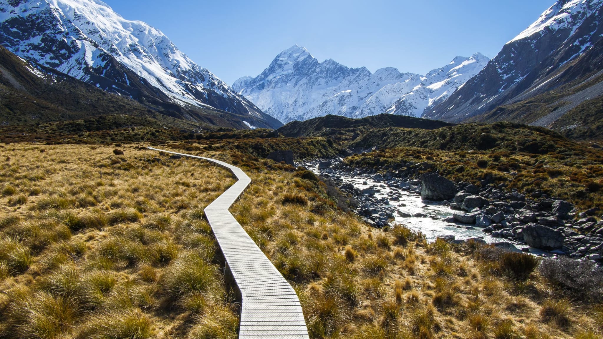 Ein Bergwanderweg in einem Tal von schneebedeckten Bergen umgeben in Neuseeland.