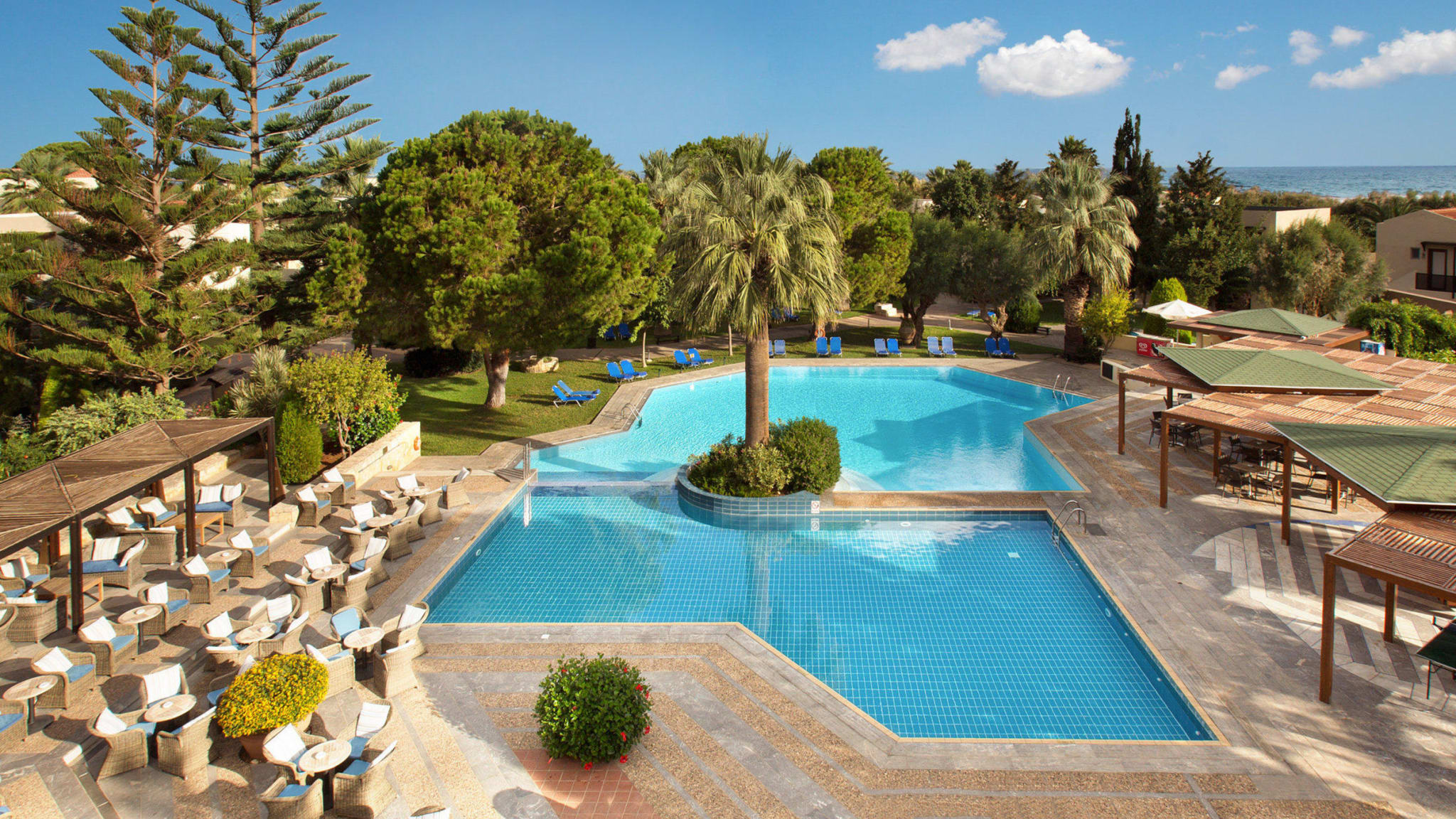 Blaues Poolbecken, Sitzmöglichkeiten, Sonnenschutz und Garten im Hotel Cretan Malia Park auf Kreta in Griechenland