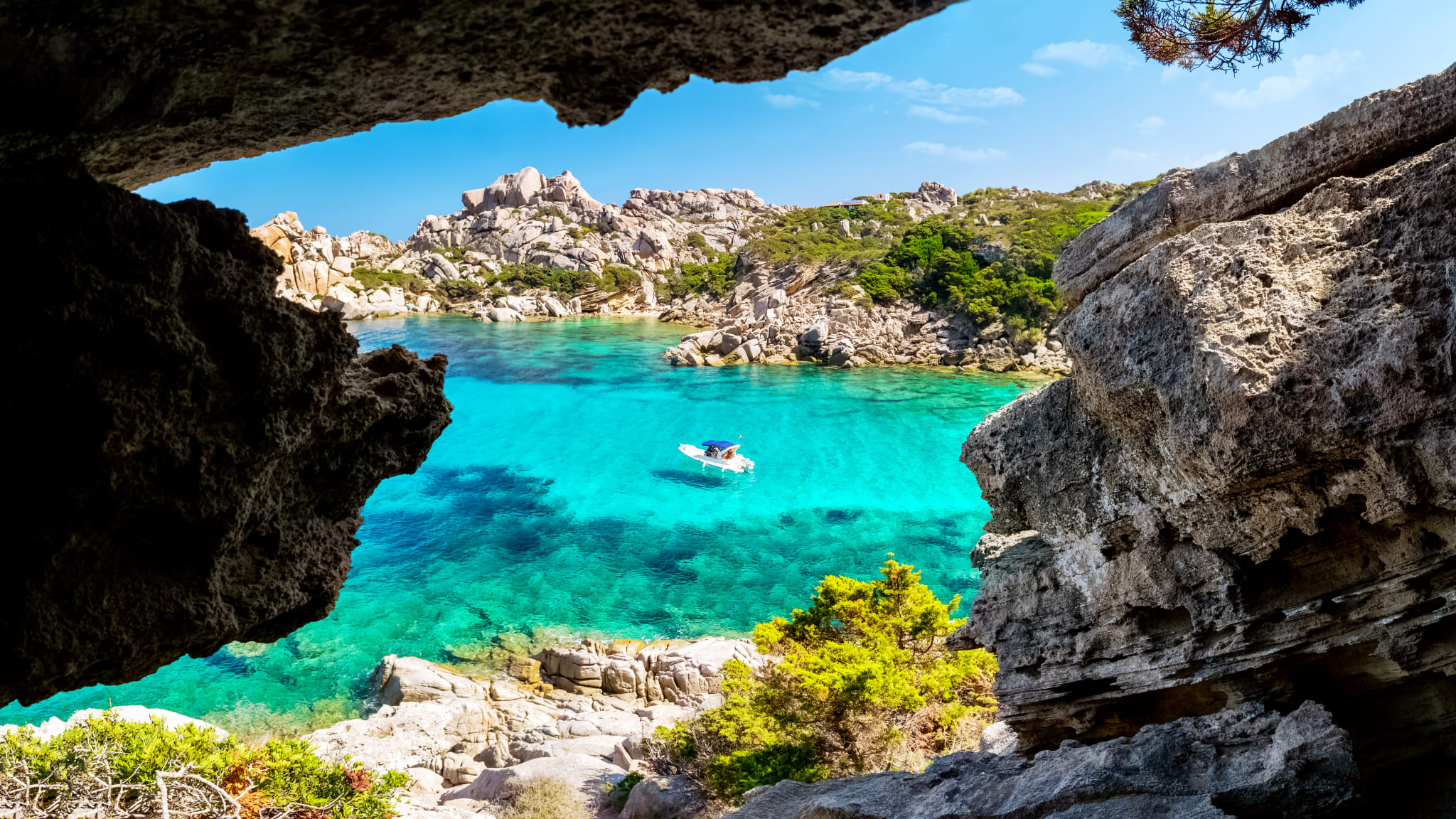 Boot auf klarem Wasser, umgeben von Felsen auf Sardinien in Italien