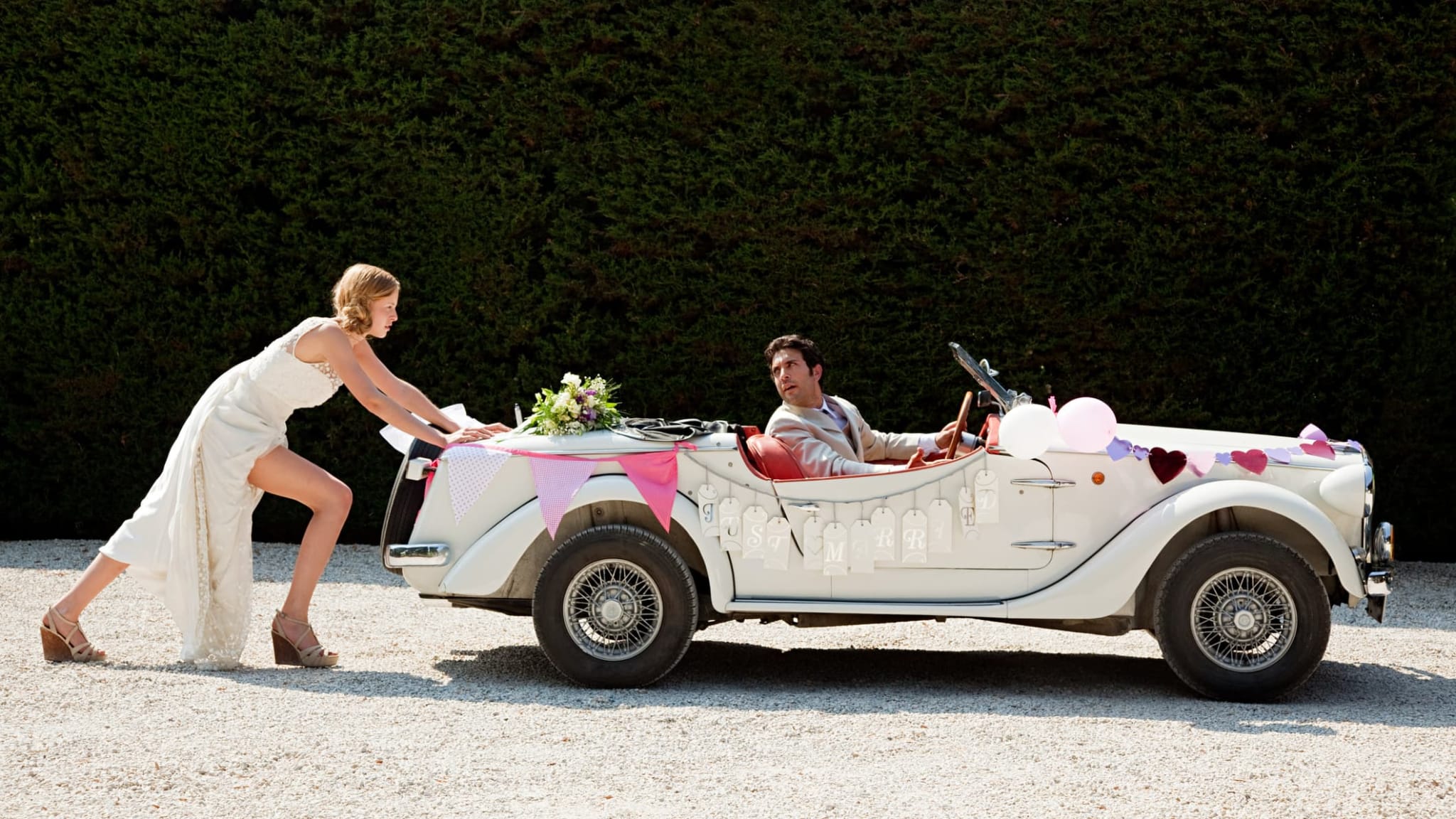 Braut schiebt kaputtes Hochzeitsauto und ist genervt.