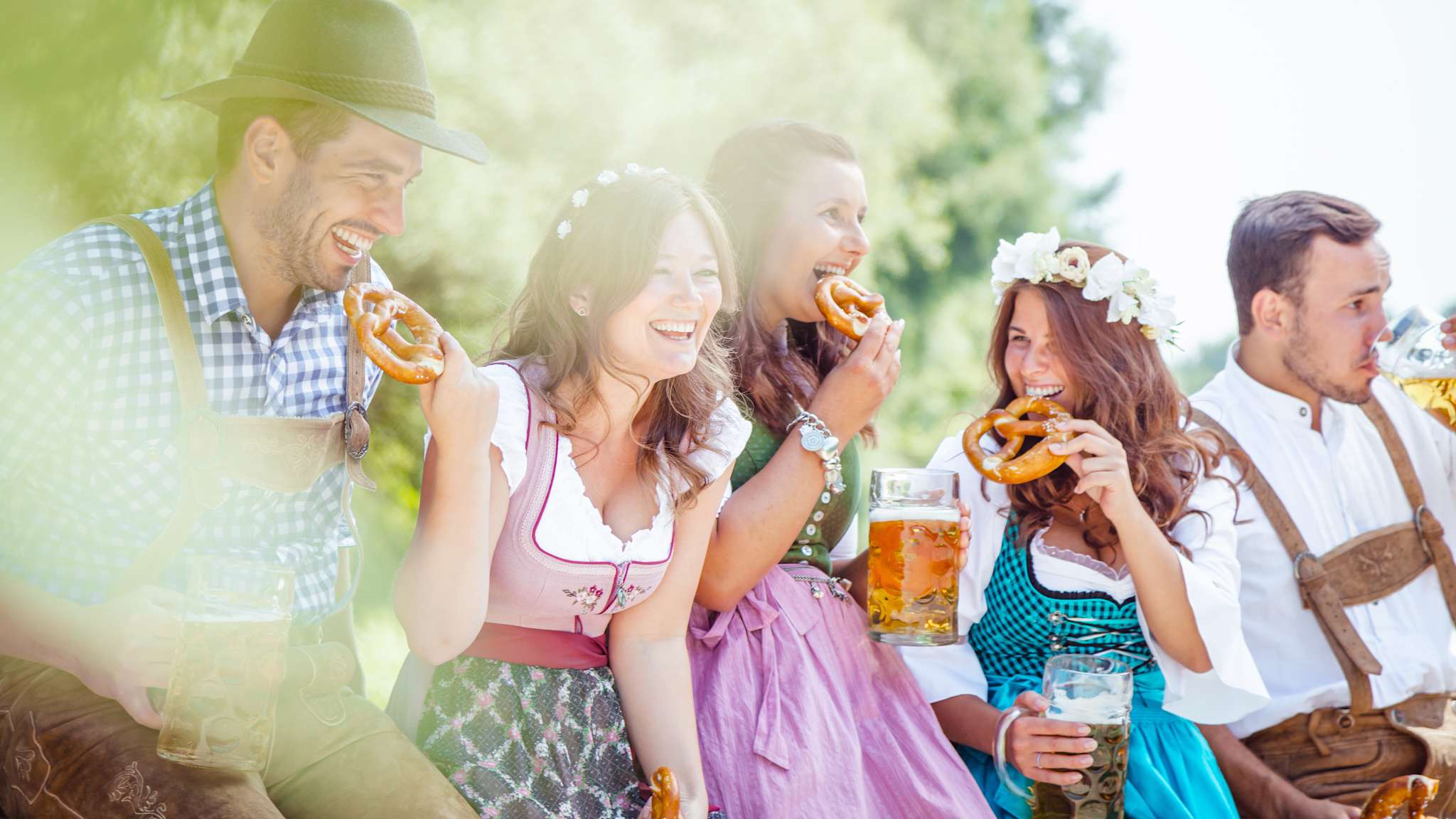 Drei Frauen und zwei Männer in Dirndl und Lederhosten drinken Bier und essen Brezeln.