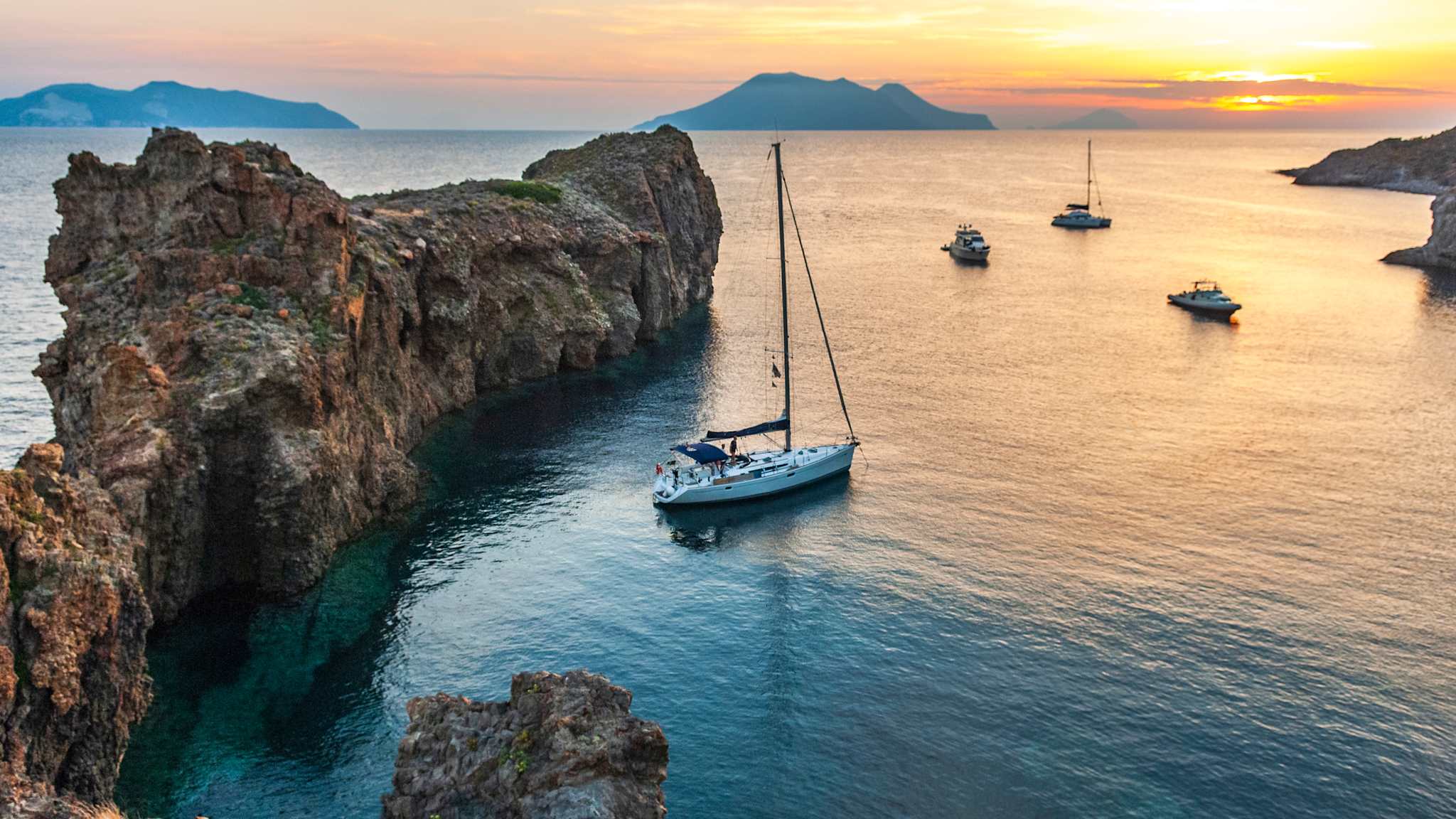 Ein Segelboot liegt vor einem Felsen im Wasser vor Anker.