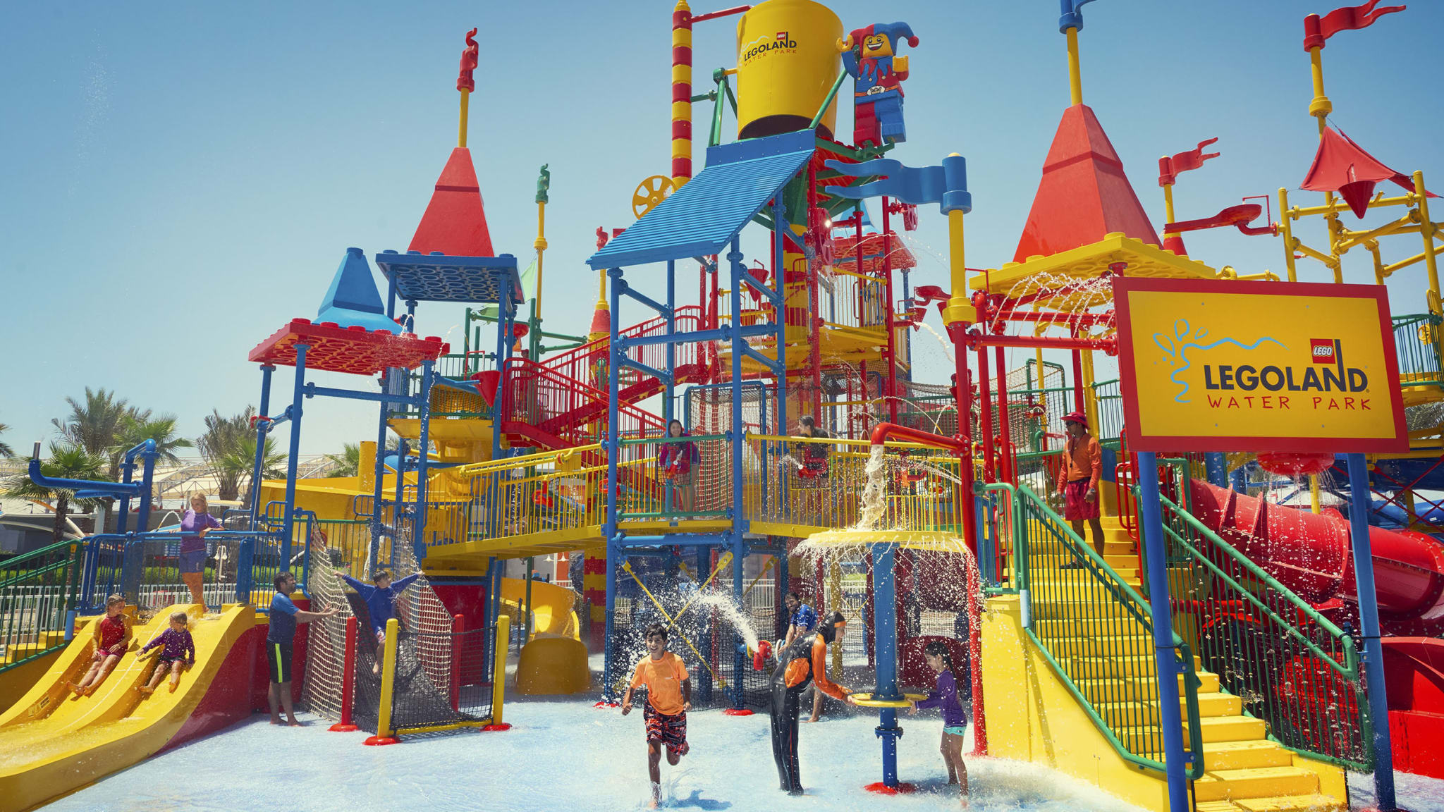 Ein buntes Klettergerüst aus Lego im Schwimmbecken, ein paar Kinder spielen darauf, überall gibt es kleine Fontänen und Wasserfälle
