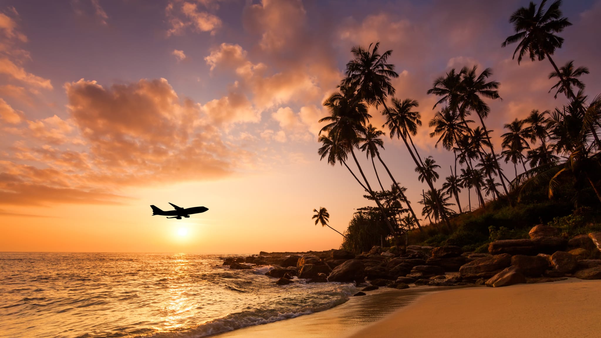 Ein Flugzeug fliegt im Abendrot über einen Strand auf den Seychellen.
